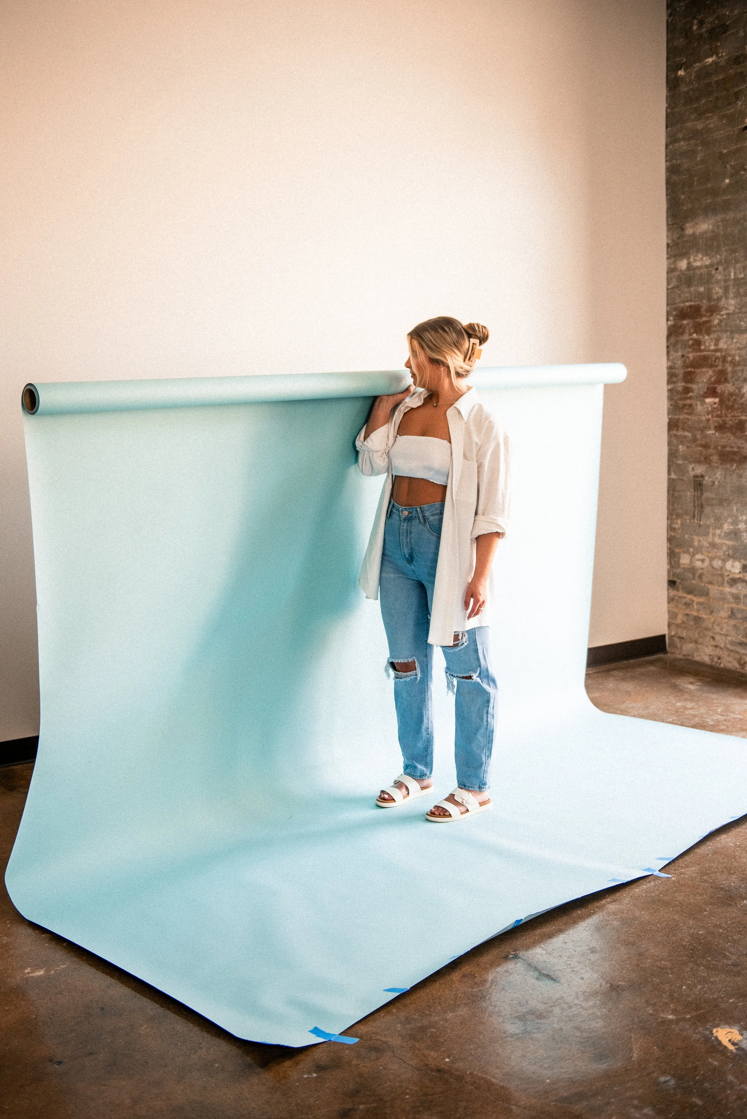 Girl standing with blue roll of background paper in alison tapp photography rental studio Gibsonville NC