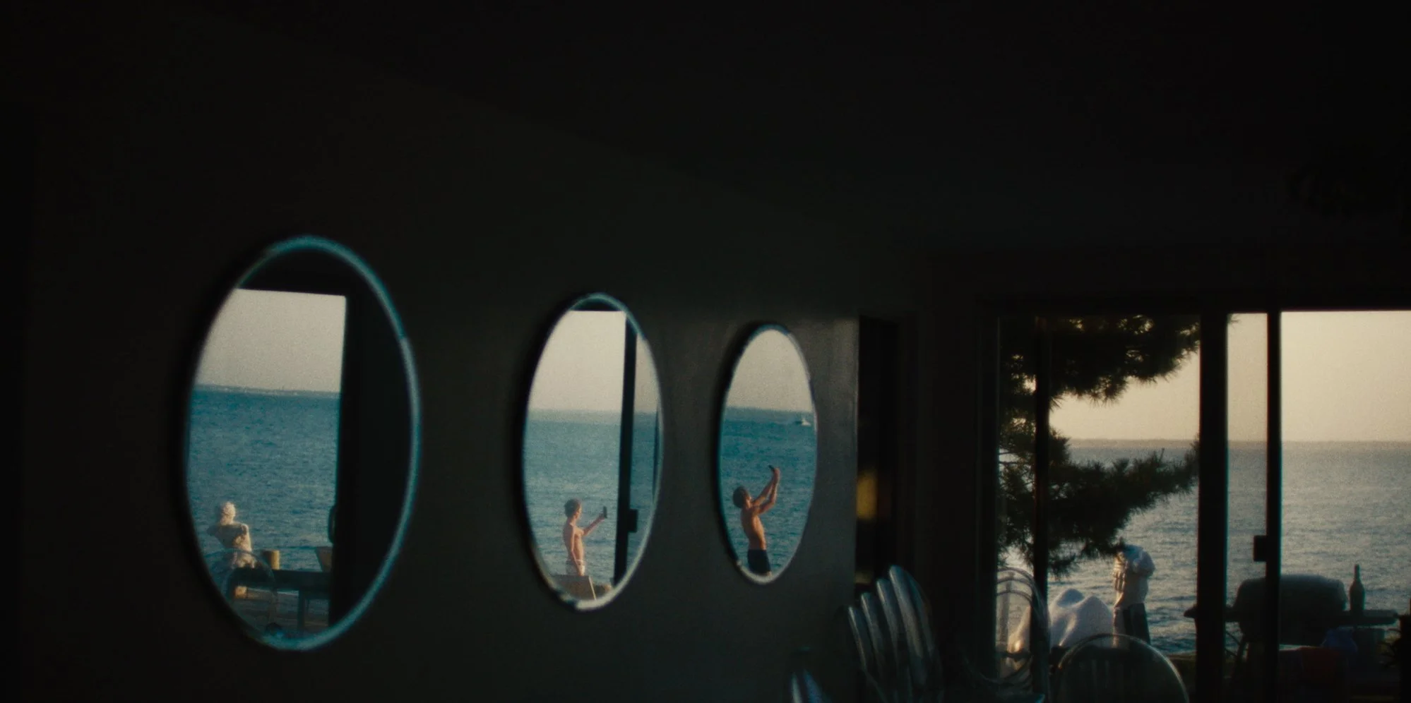 View of a seaside scene through porthole windows with people on the deck and a person doing yoga.