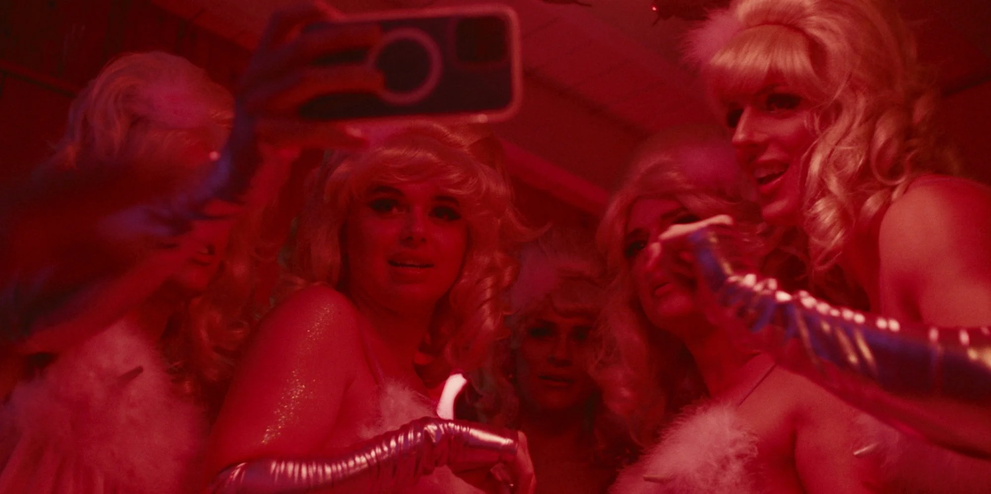 Group of women with blonde hair and festive costumes taking a selfie in a red-lit environment.