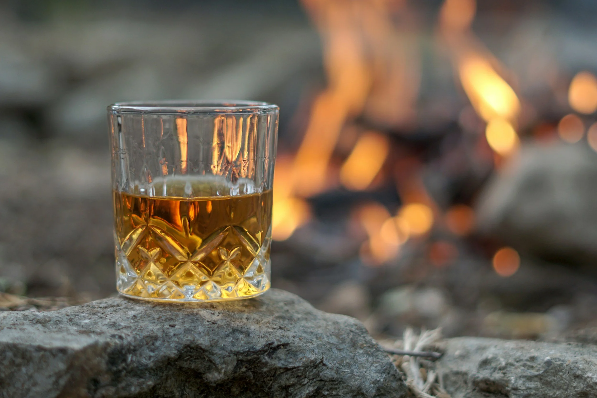 cut glass of bourbon with a campfire in the background.