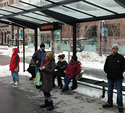 Riders wait at a new Kennedy Plaza bus stop. A sign offering real-time bus information is included at each new shelter in the plaza.