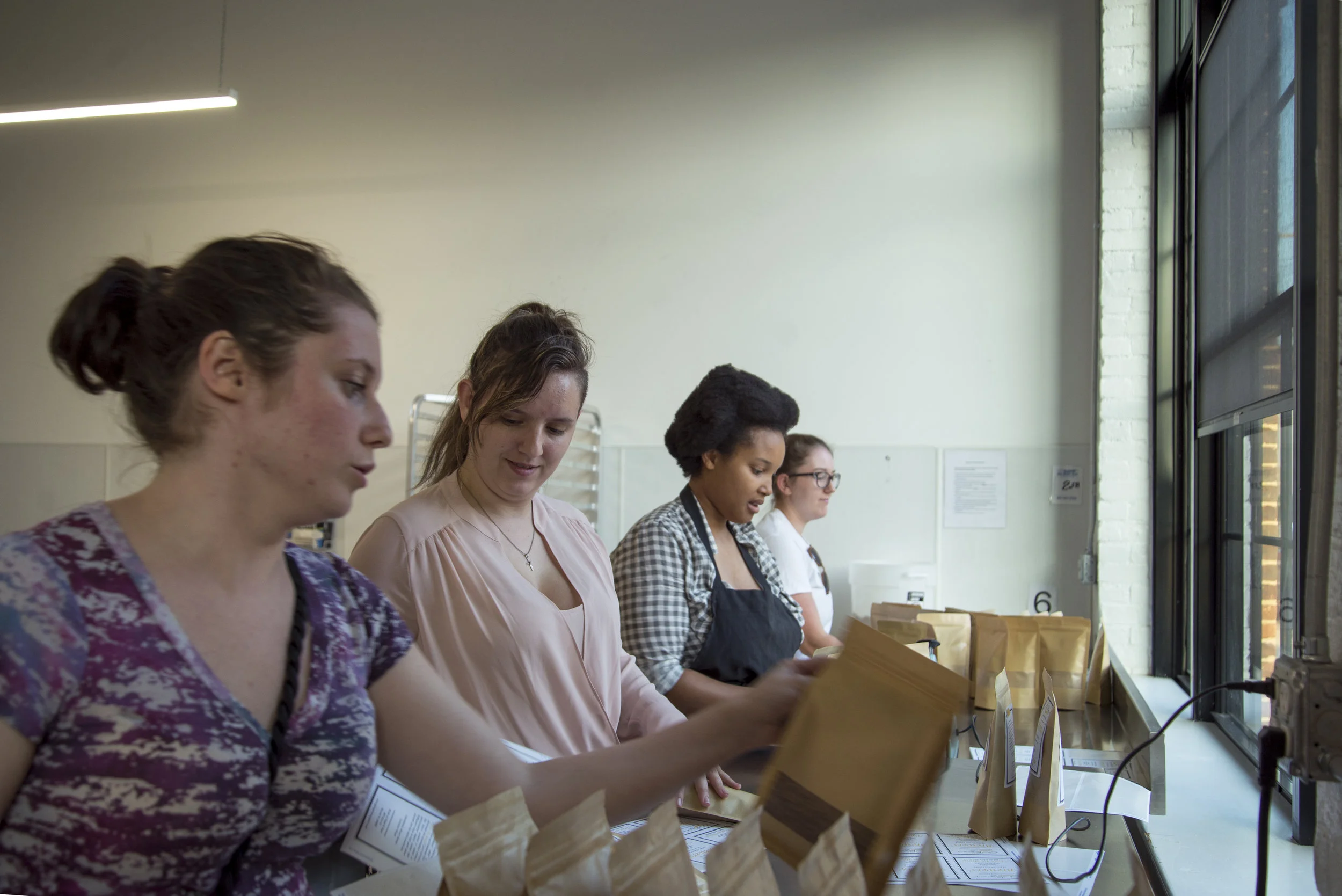 From left, Sam Gannon, Jessie Pulling, Natasha Daniels, and Nicole Gresko work, assembly-line style, to pack and label OURgrain flour, which is made from brewers’ spent grain. (Joanna Detz/ecoRI News)