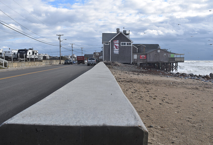 A seawall along a road and a beach.