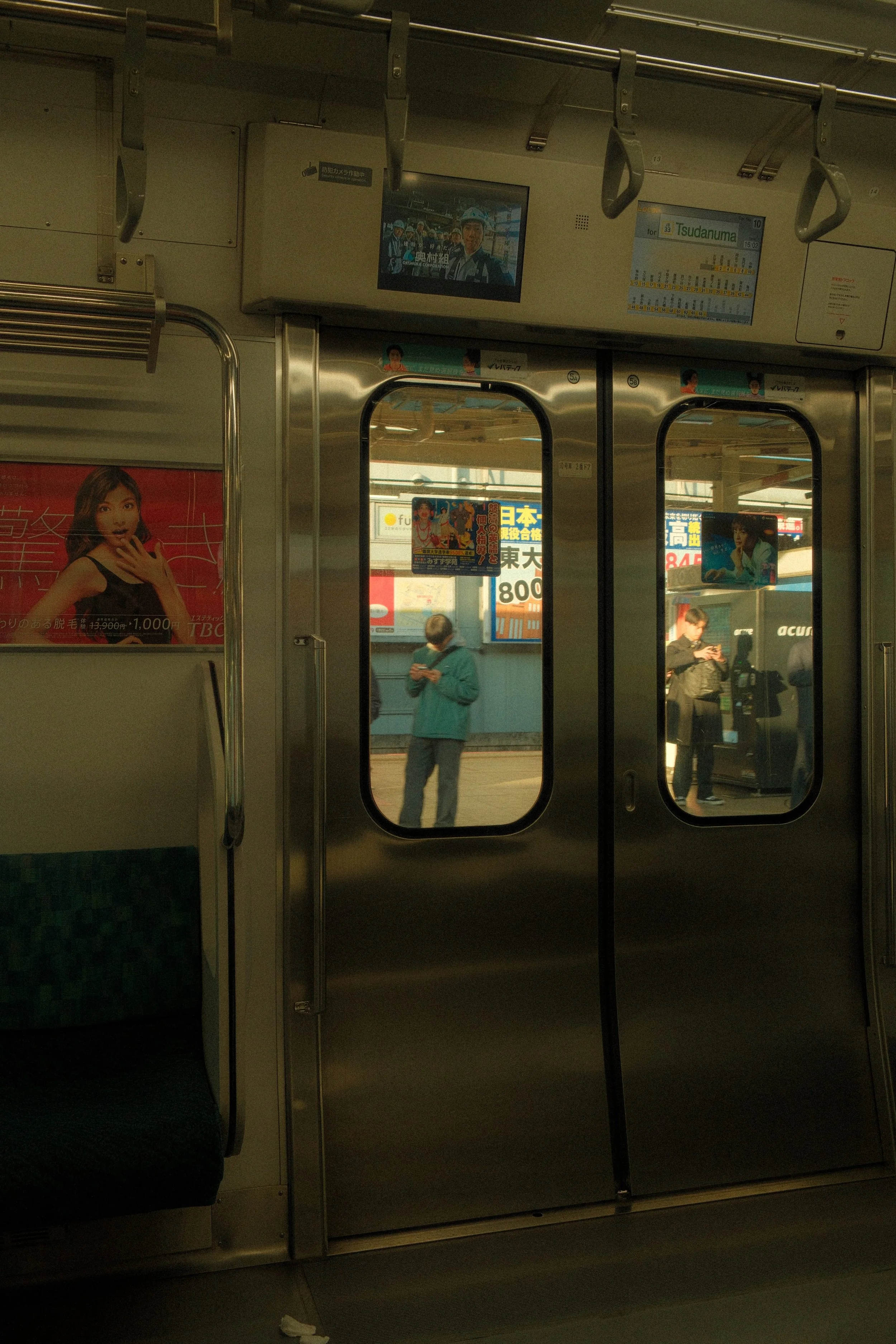 Inside a train, view of passengers standing outside at a train station, reflected in glass doors.