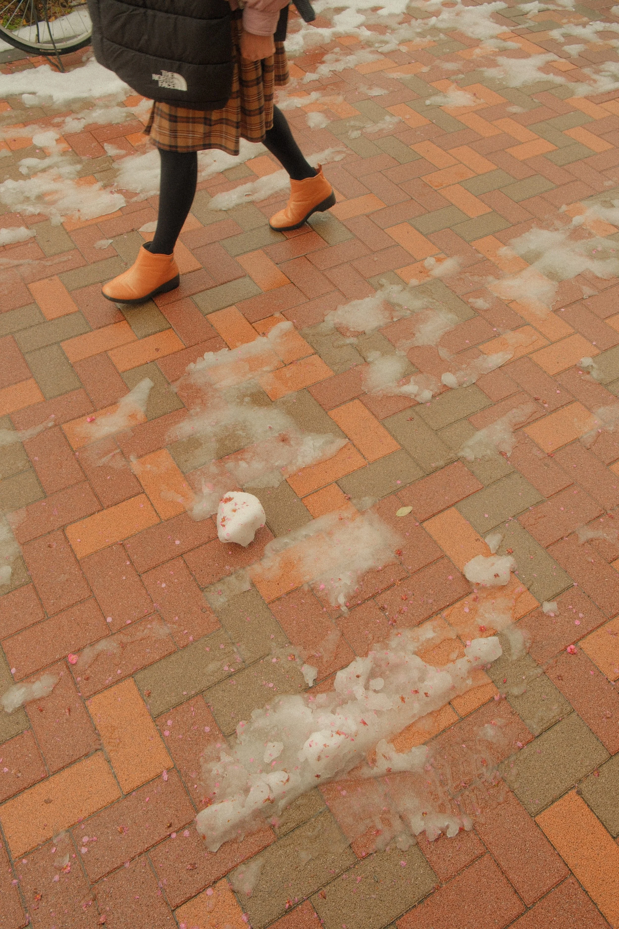 A person walking on a brick sidewalk with snow and cotton candy remnants scattered on the ground.