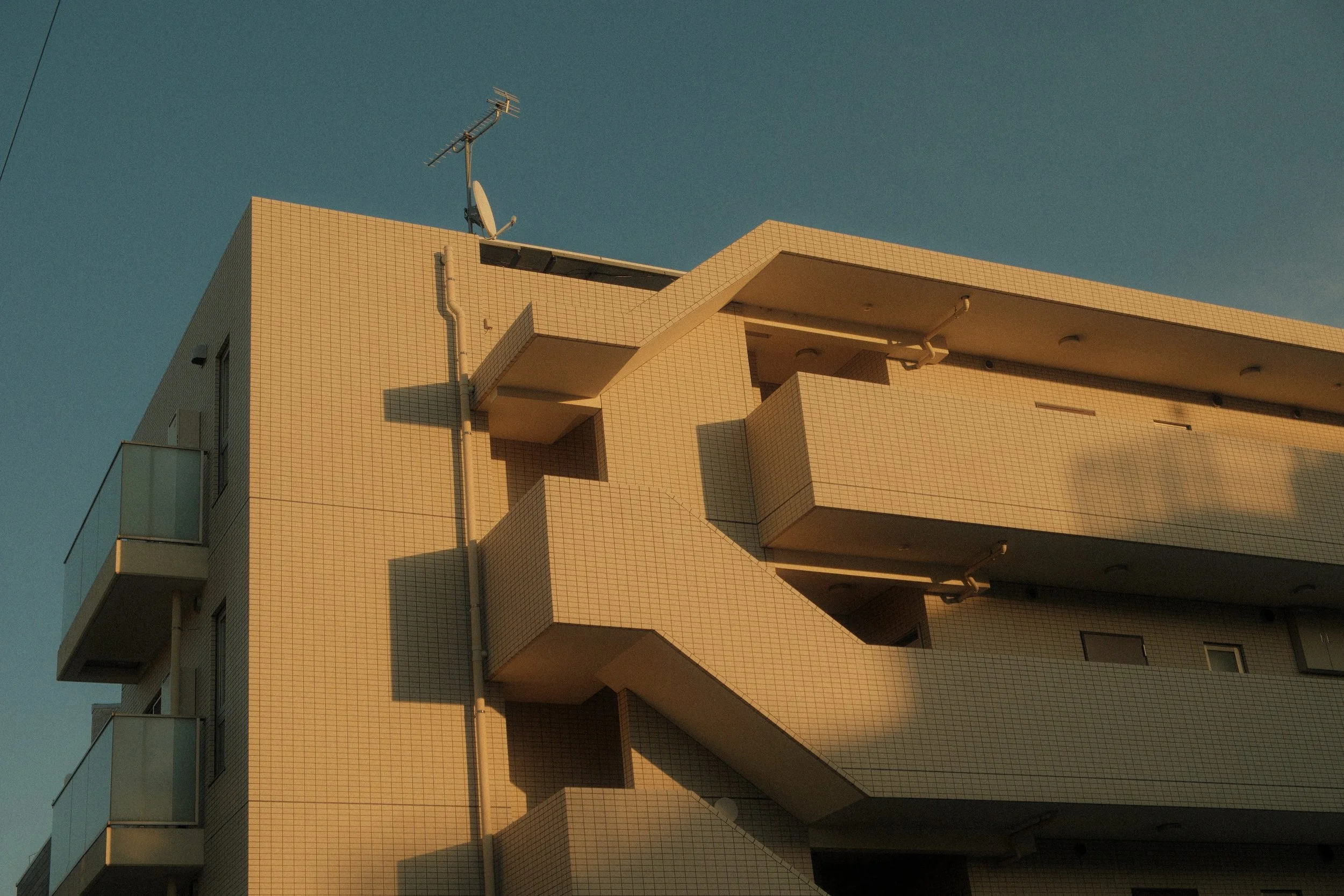A multi-story apartment building with beige tiled exterior and balconies under a clear sky.