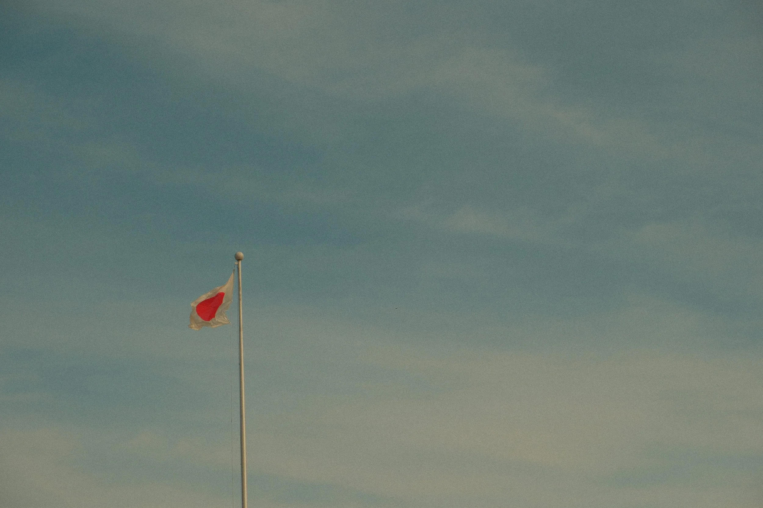 A Japanese flag waving on a flagpole against a cloudy sky.