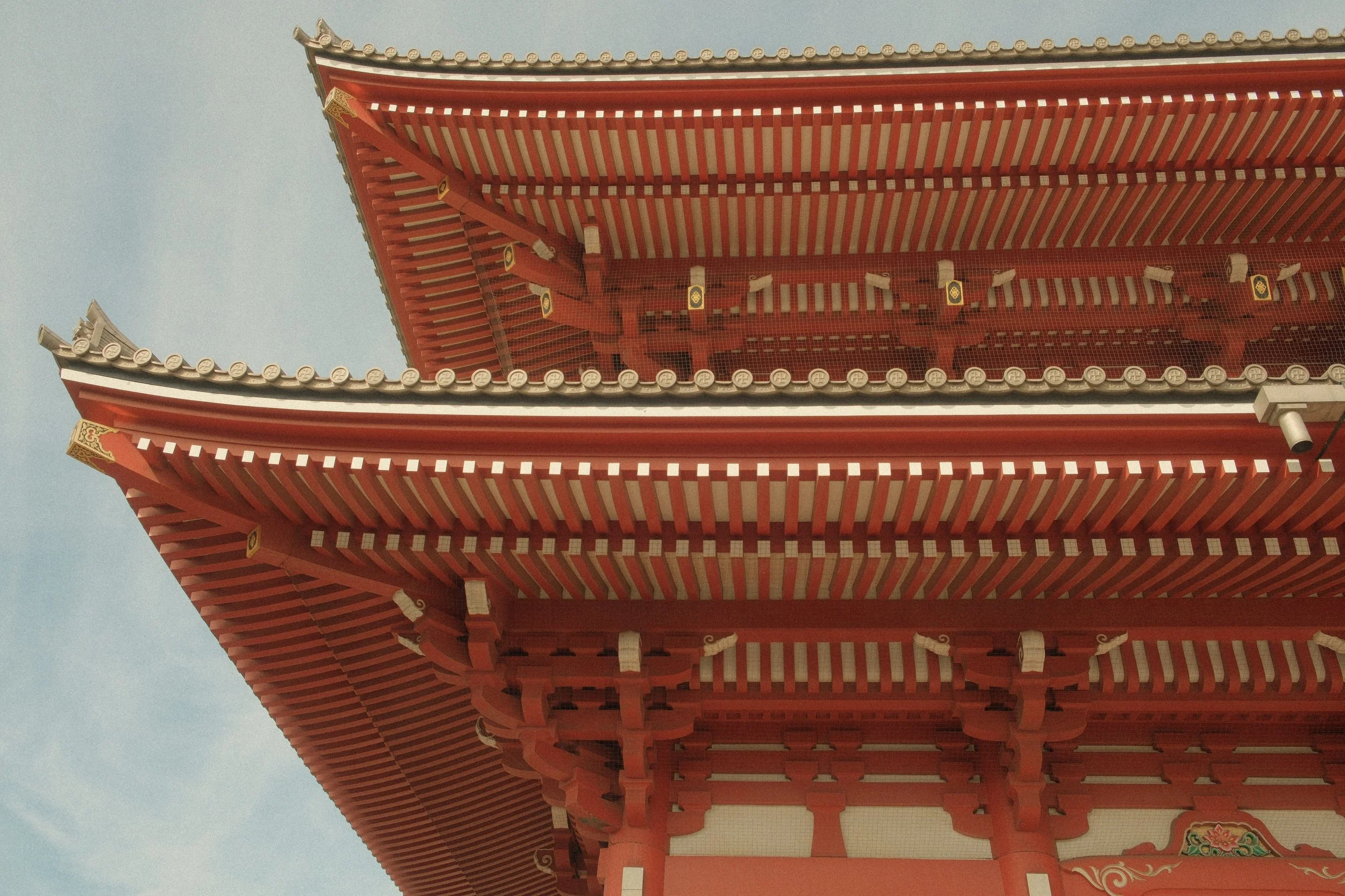 Close-up of a traditional Japanese temple's red wooden roof with intricate design and decorative elements.
