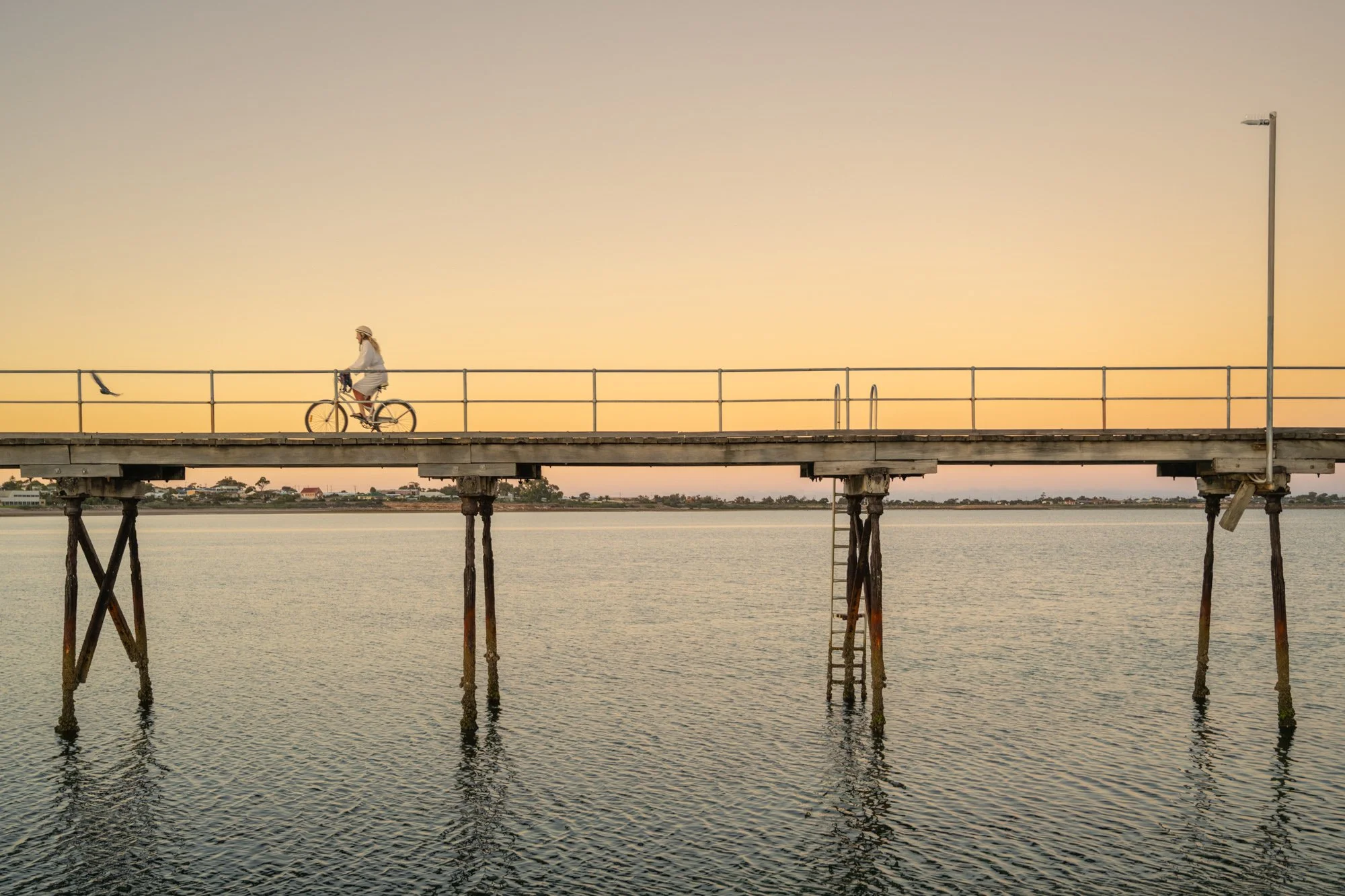 lady in dressing gown riding bicycle on jetty at sunrise