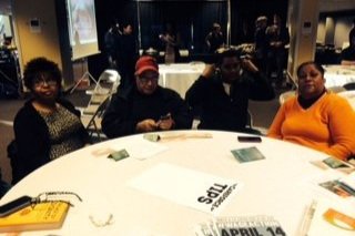  People sitting around tables in a dining room smiling. 