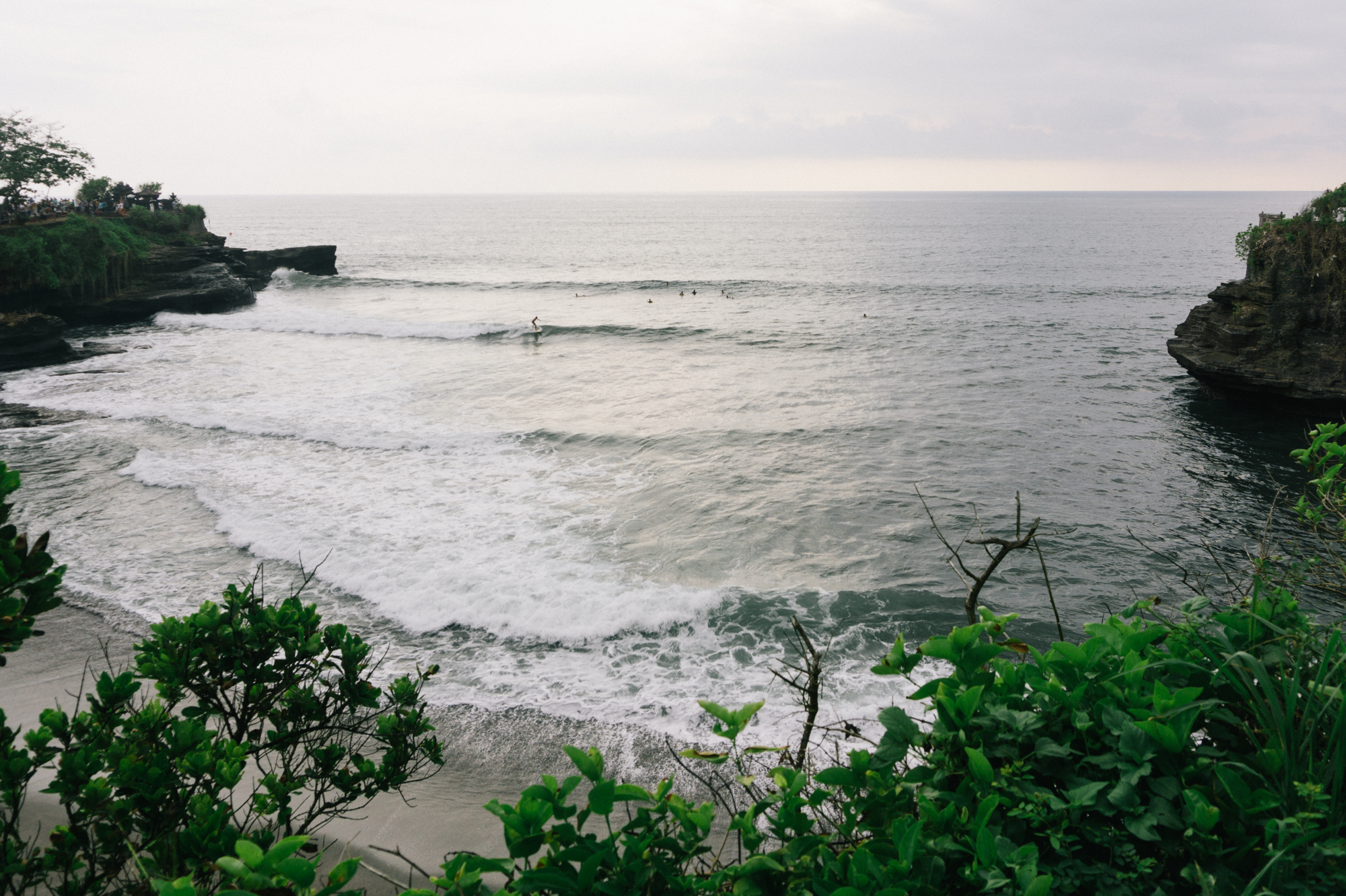 Surfers take advantage of the waves between the two temples of Tanah Lot, Bali.