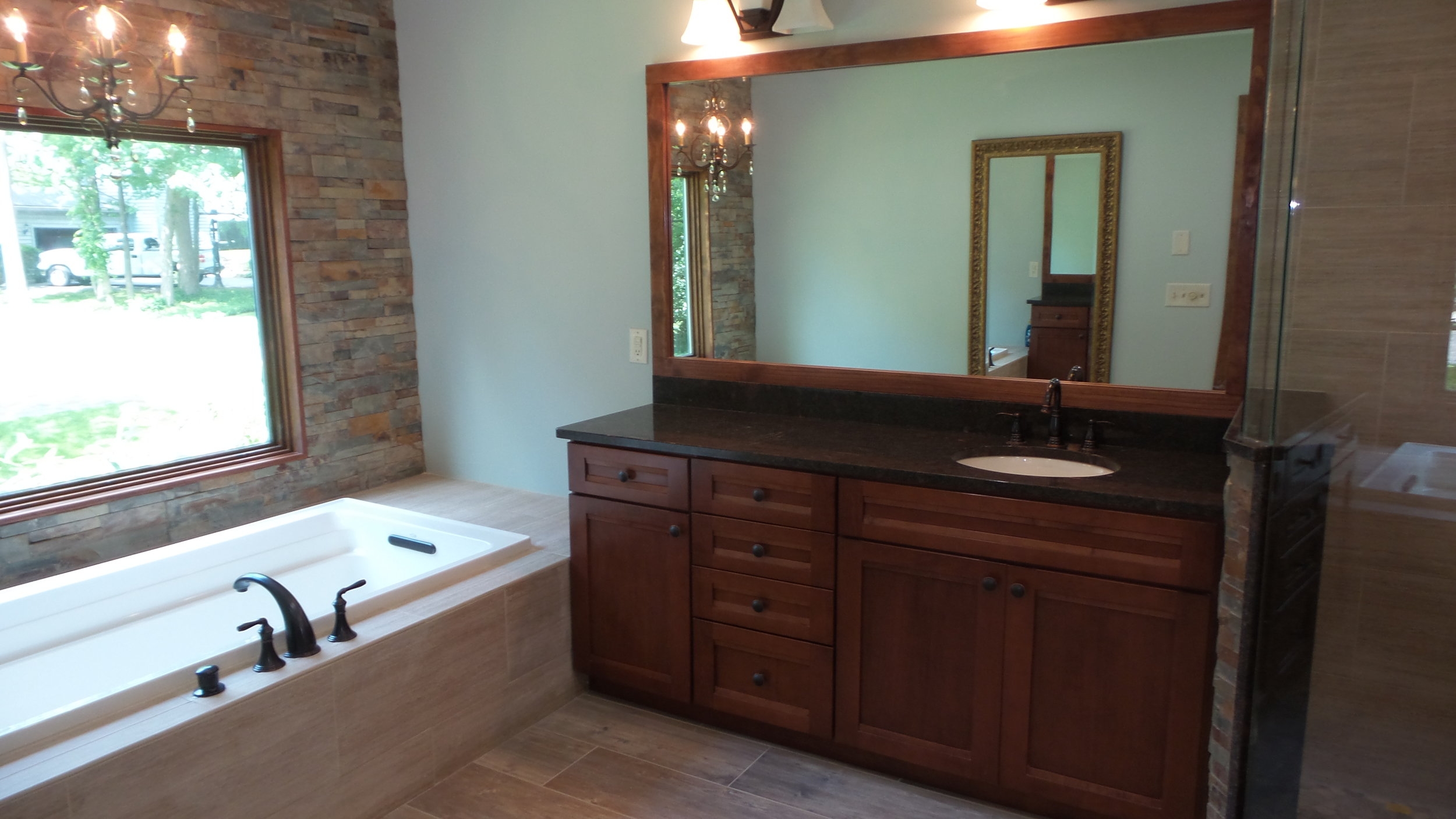 Luxury bathroom with new tub, tile, mirror, chandelier, recessed lights and a stone wall feature.