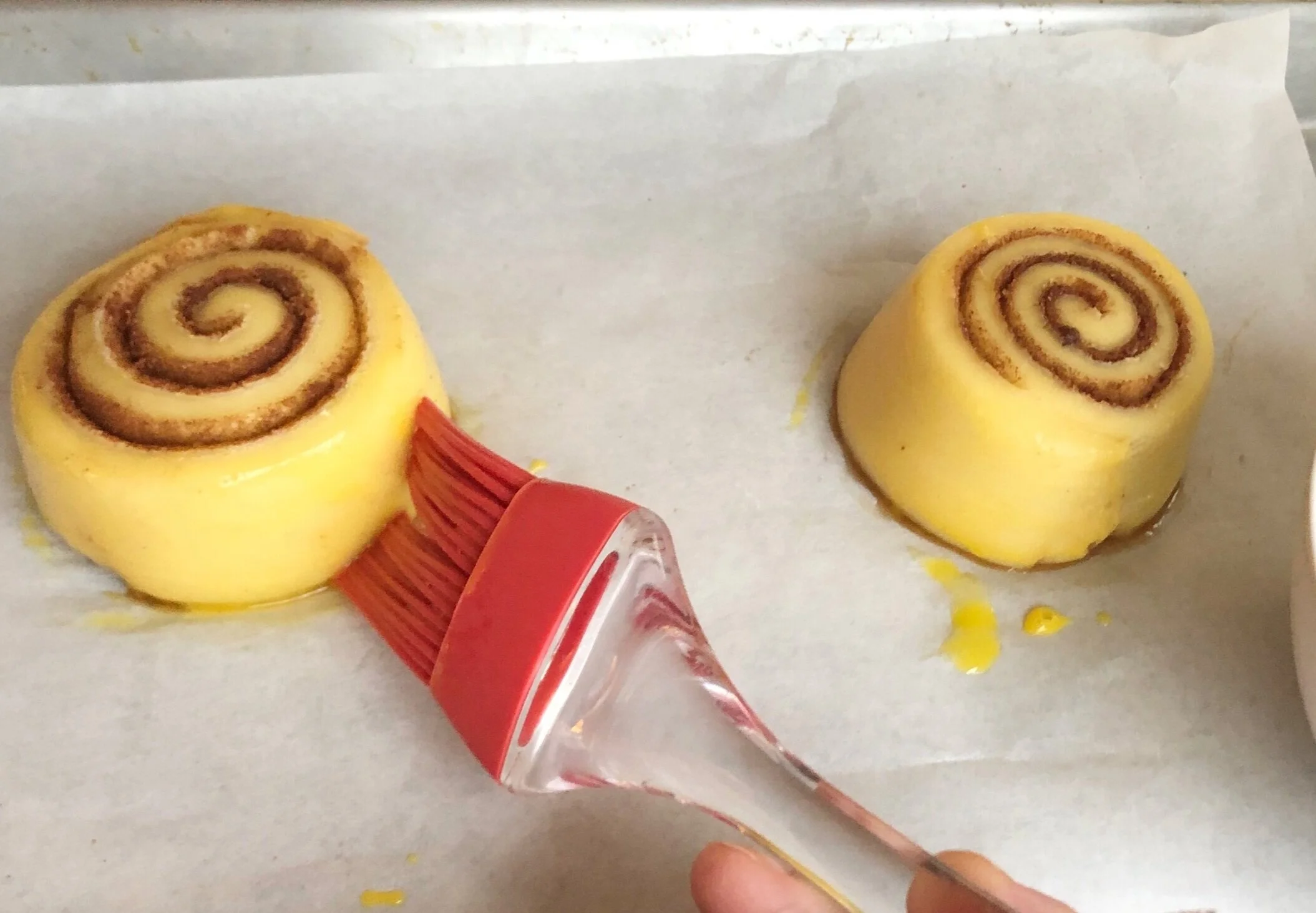 Fully proofed cinnamon rolls getting an egg wash before baking.