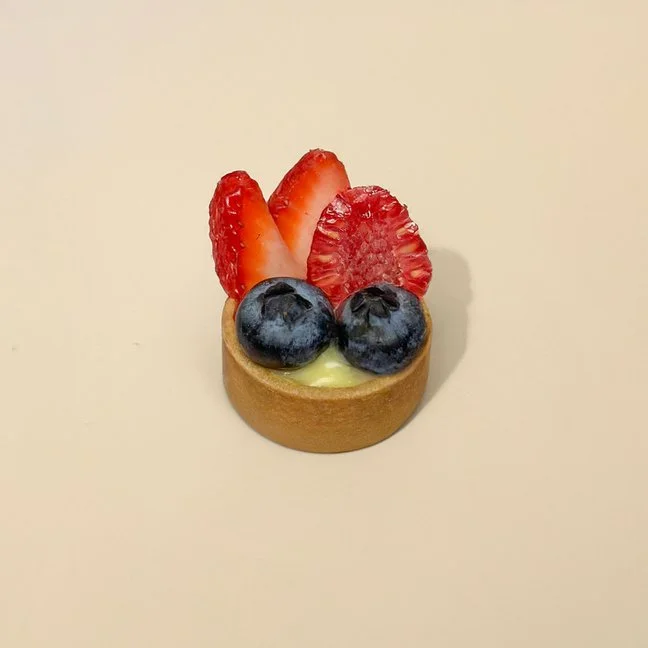 Mini fruit tart with strawberries, blueberries, and a yellow filling on a plain beige background.