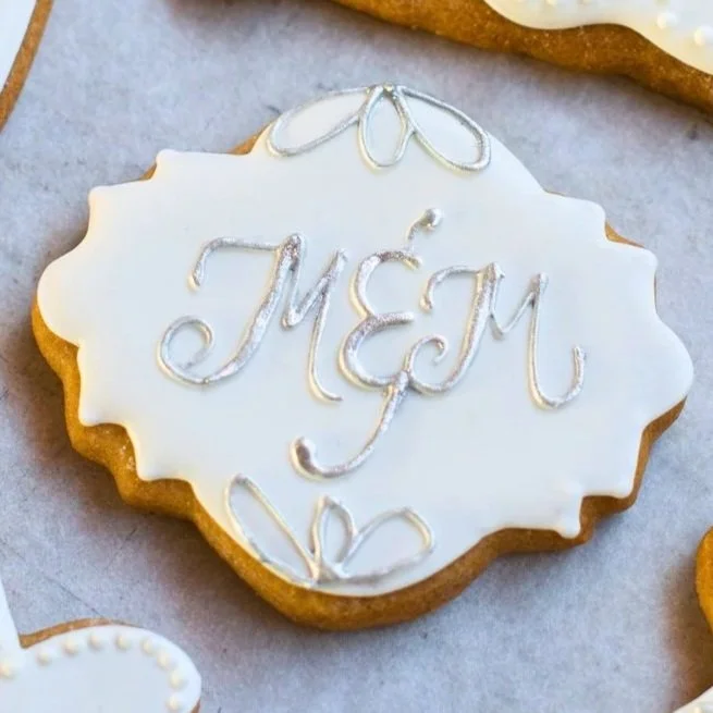 Decorated sugar cookie with white icing and silver writing that says 'MOM' and floral designs