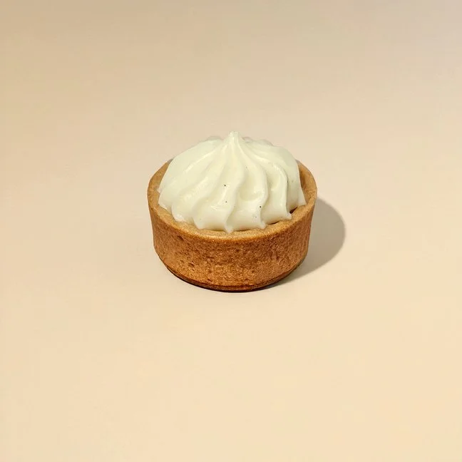 Lemon tart with whipped cream topping on a plain light-colored surface.