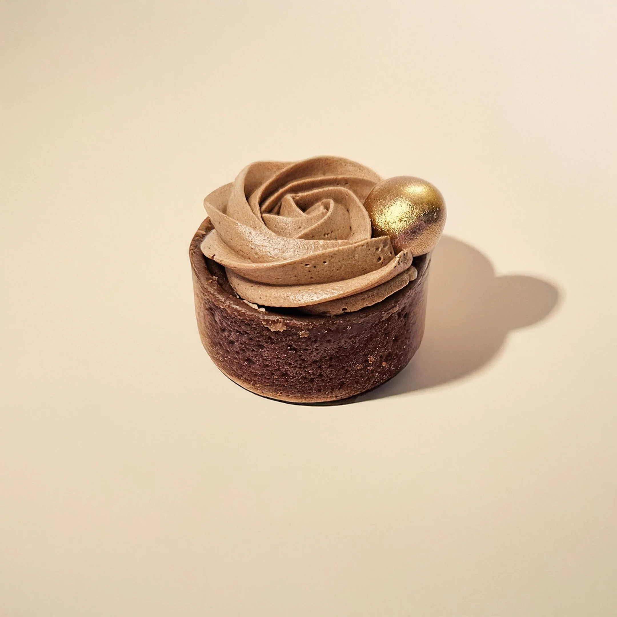 Chocolate cupcake with decorative swirls of chocolate frosting, topped with a gold-colored spherical ornament.