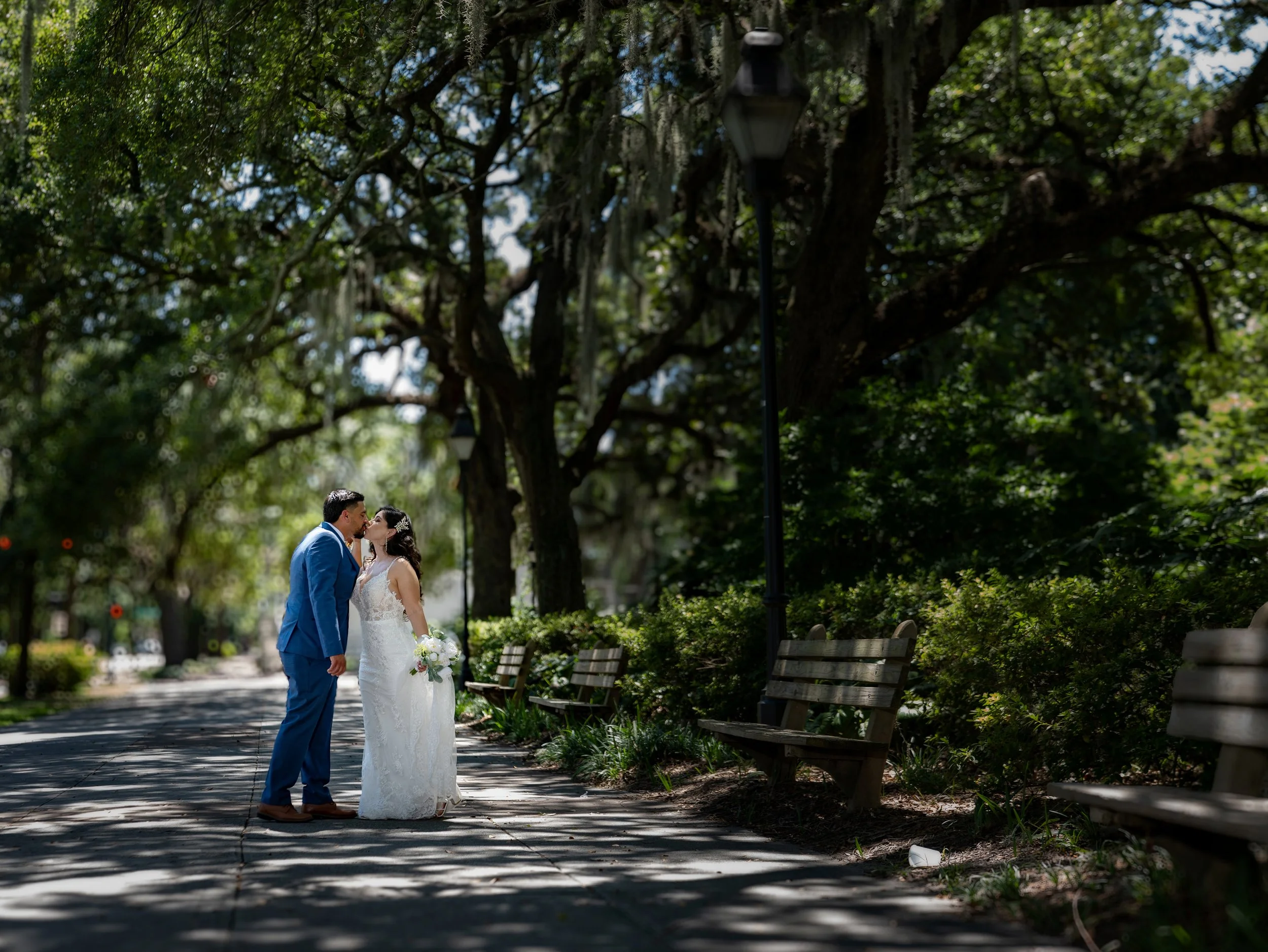 Bride and groom kissing beneath live oak trees in the mid day sun at Forsyth Park Savannah.