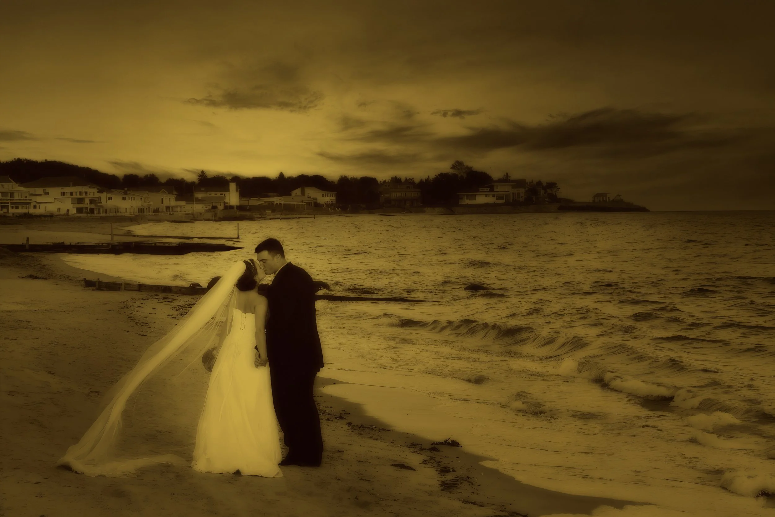 Bride and groom kissing on the shoreline at Water’s Edge Resort & Spa in Westbrook, Connecticut.