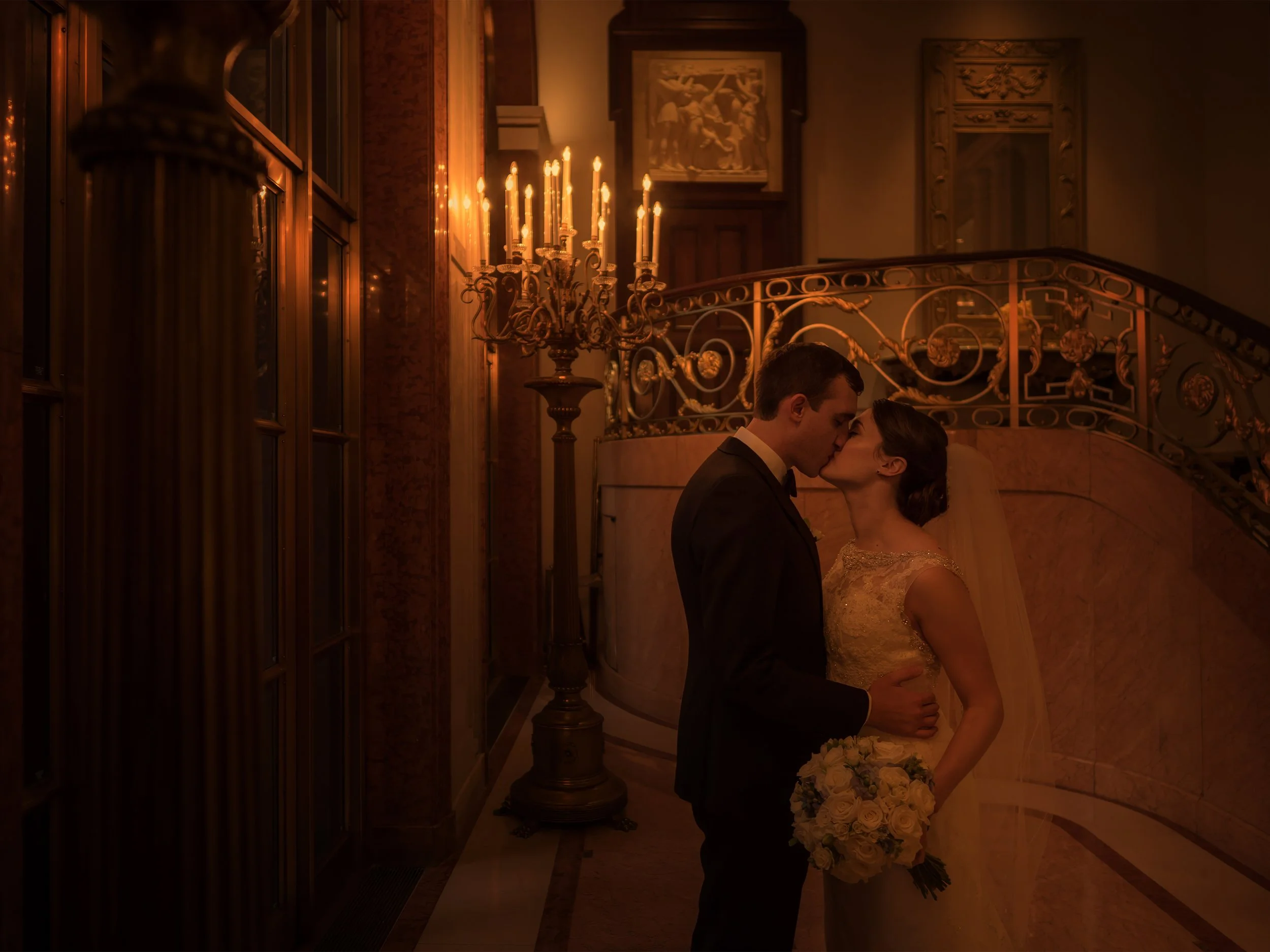 Bride and groom kissing in the warm glow of the foyer at Lotte New York Palace Hotel in New York City.