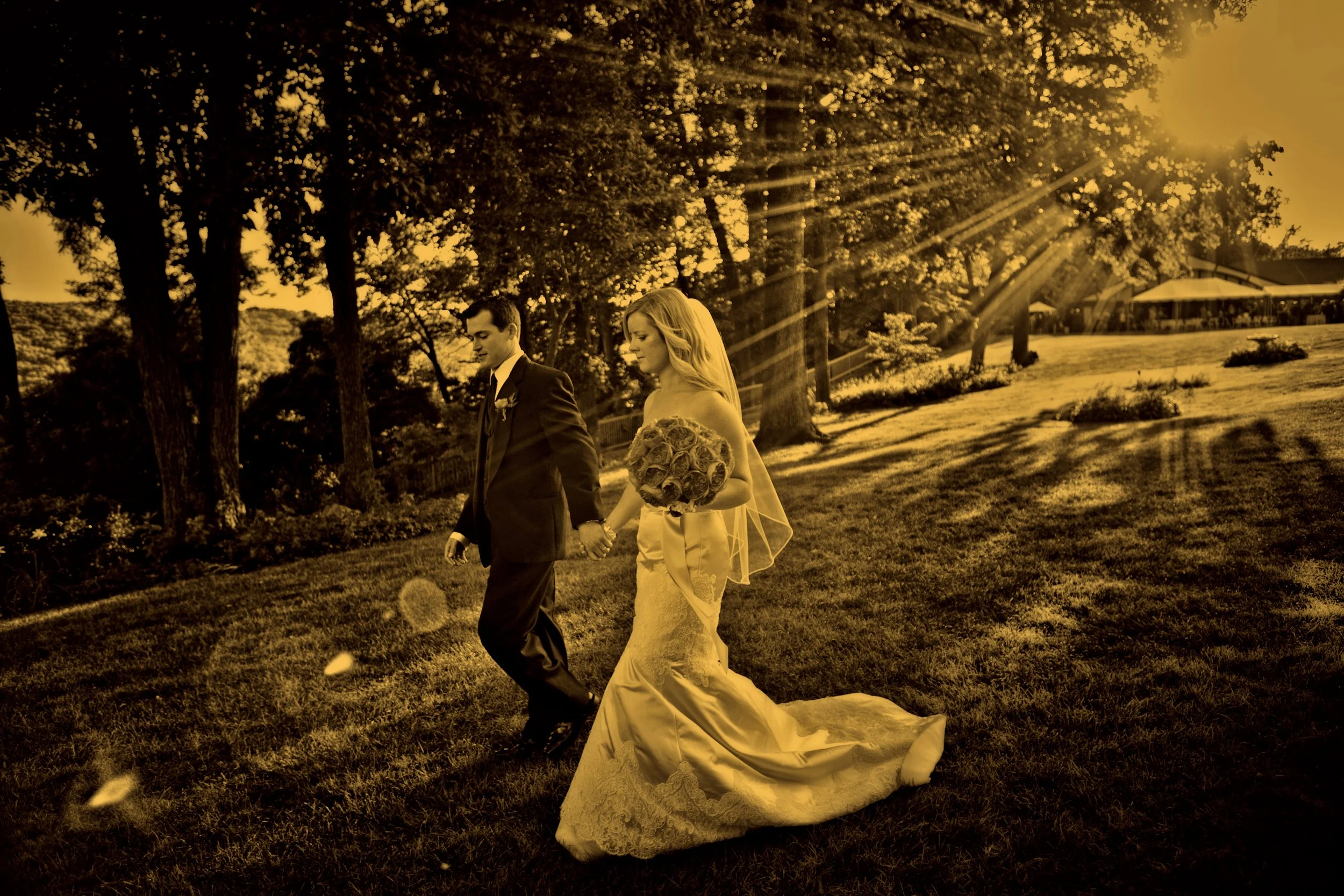 Fine art split toned photograph of bride and groom walking on the grounds of Saint Clements Castle with sunlight sparkling through the trees.