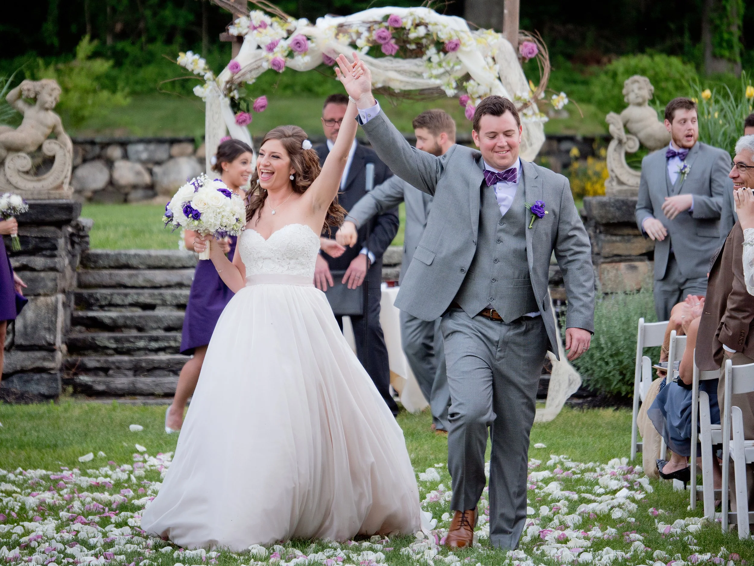 Bride and groom raising their hands in celebration during their ceremony recessional in the sunken gardens at Saint Clements Castle.