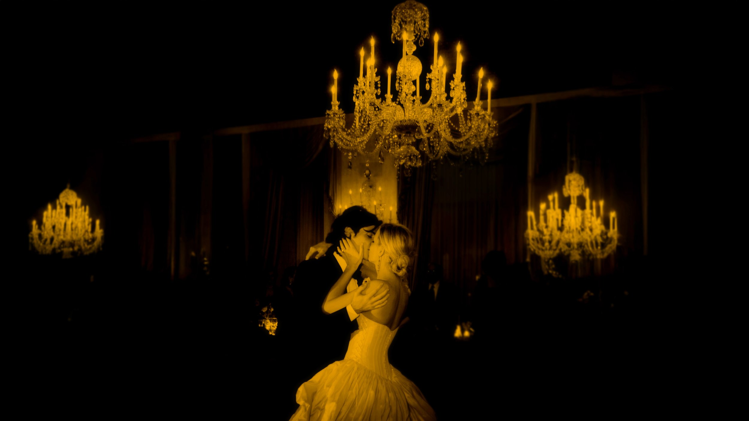 Bride and groom kissing beneath crystal chandeliers during a ballroom wedding reception at The Harmonie Club in New York City.