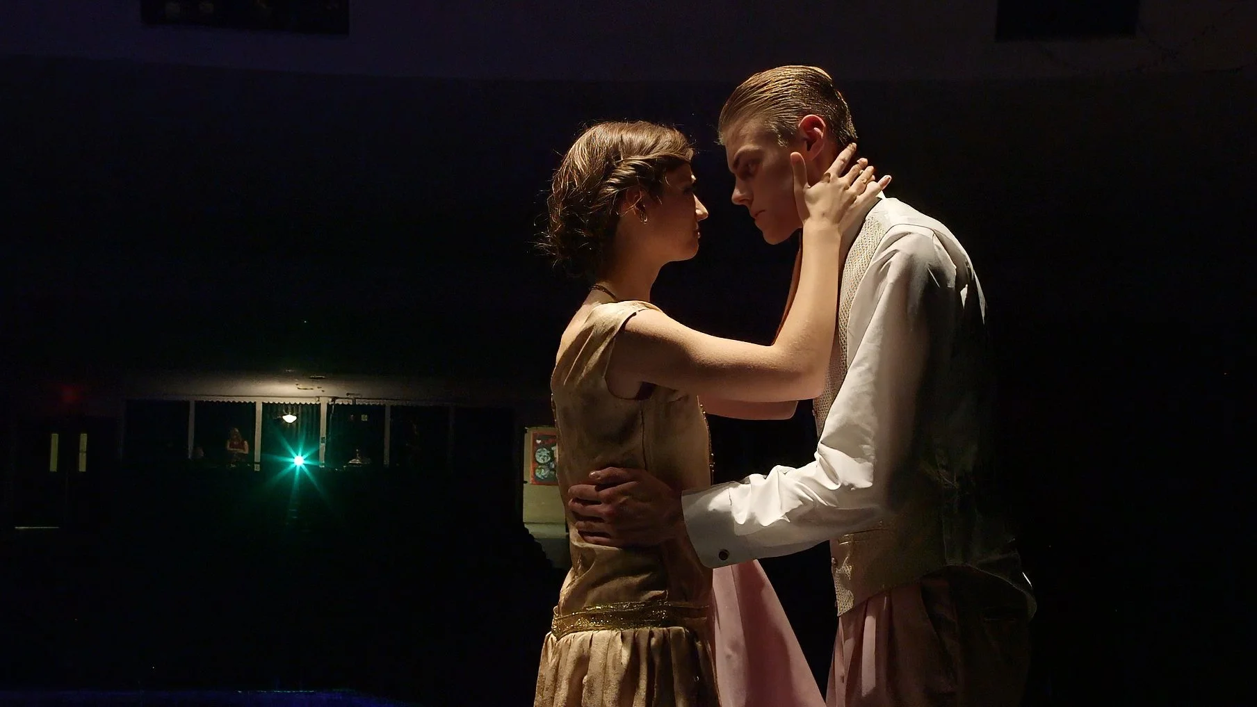 Two actors embrace beneath dramatic theatrical lighting during Sheehan High School's stage production of The Great Gatsby.