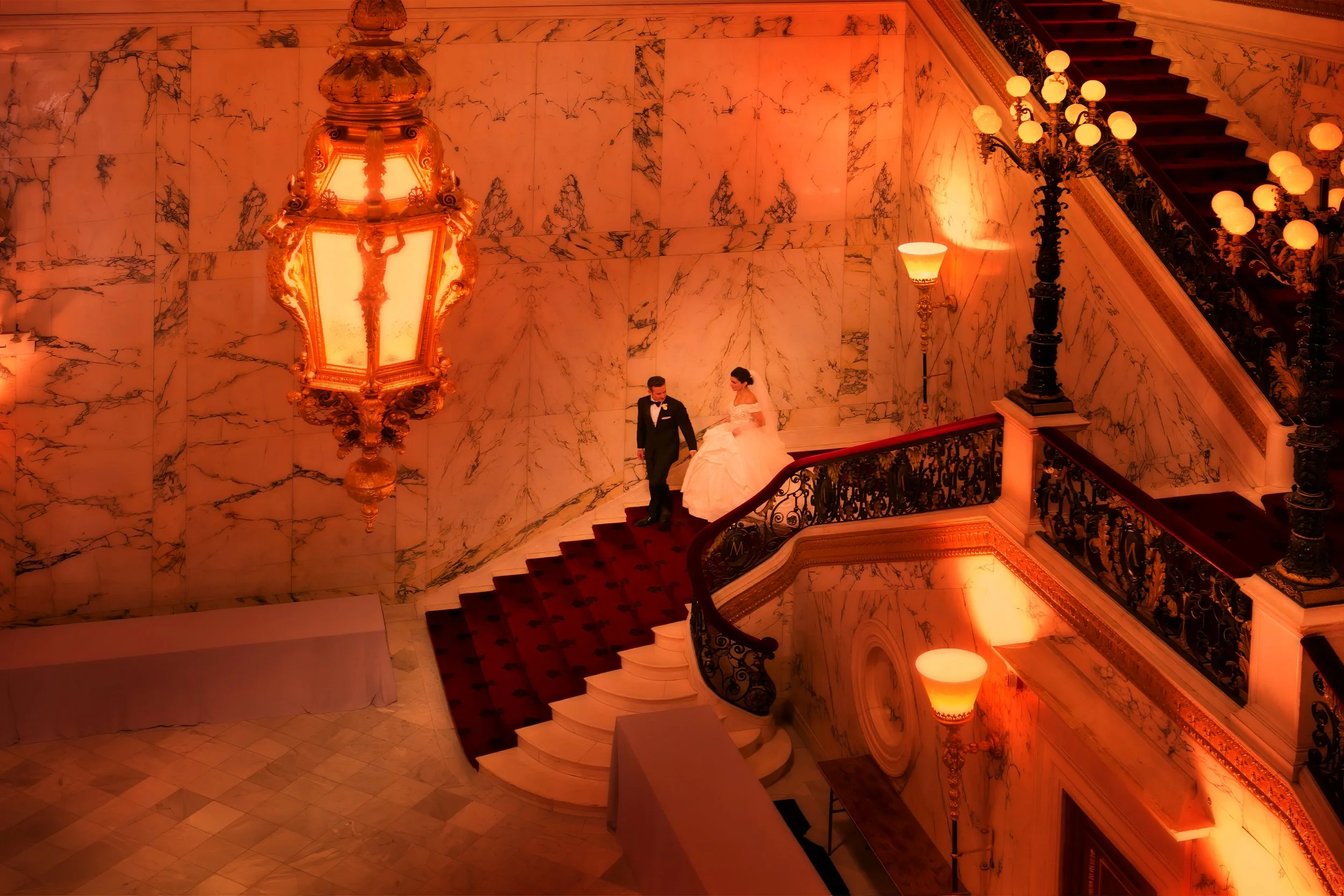 Bride and groom descending the grand staircase at the Metropolitan Club, captured in soft, romantic lighting.
