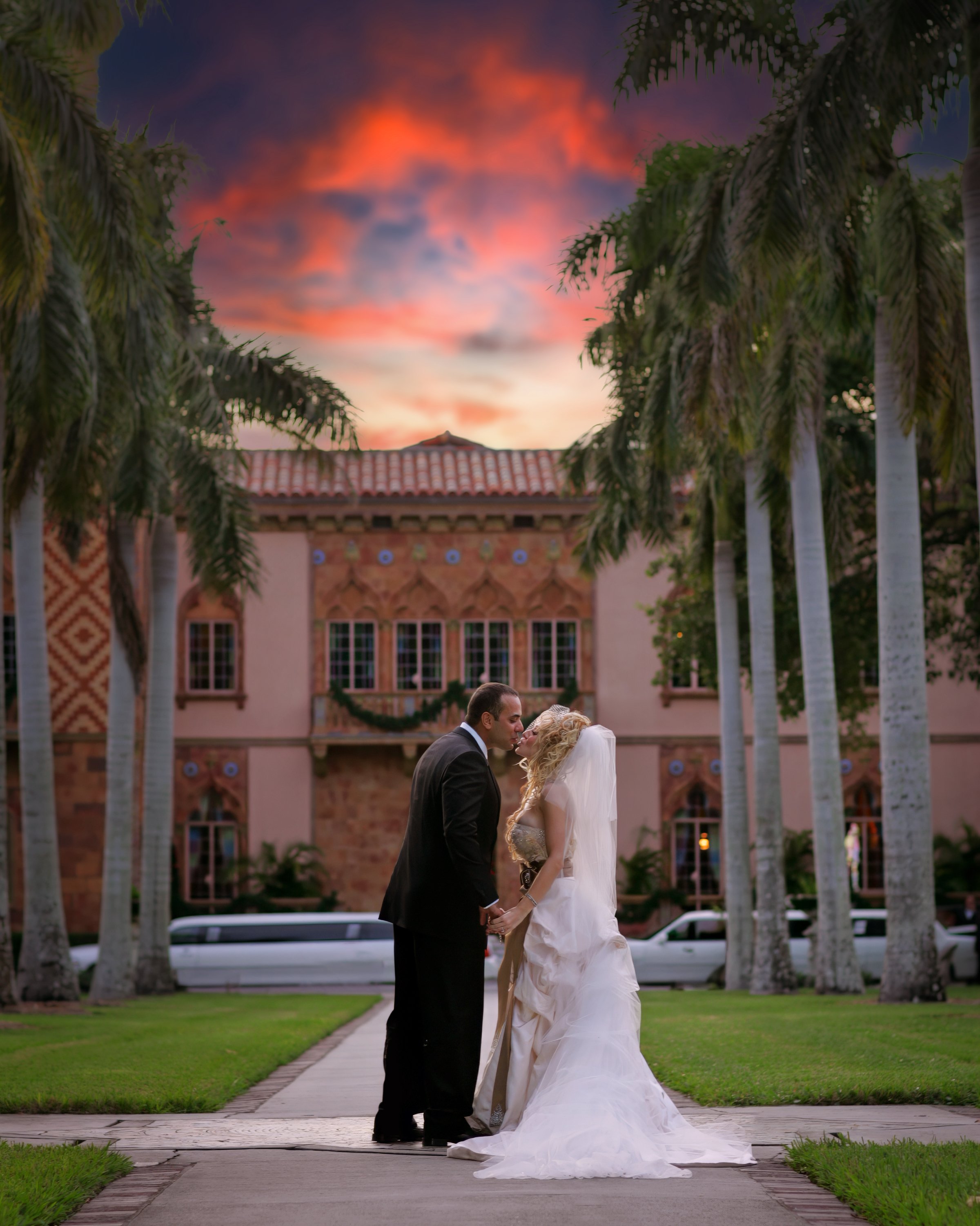 Bride and groom sharing a kiss with the Ringling Museum and vintage wedding limousines in the distance