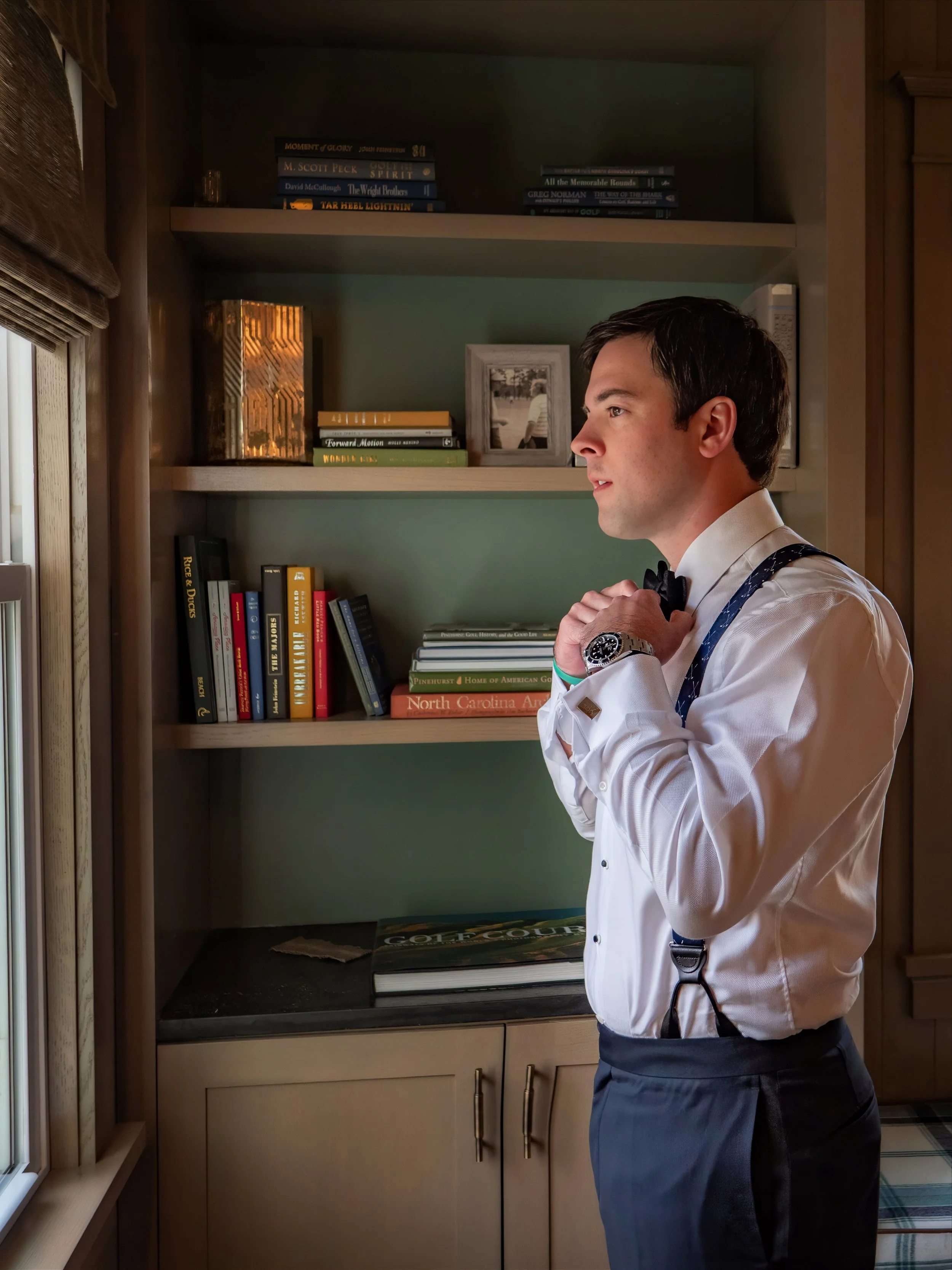 Groom adjusts his bowtie as he prepares for his wedding day at The Manor at Pinehurst Resort.