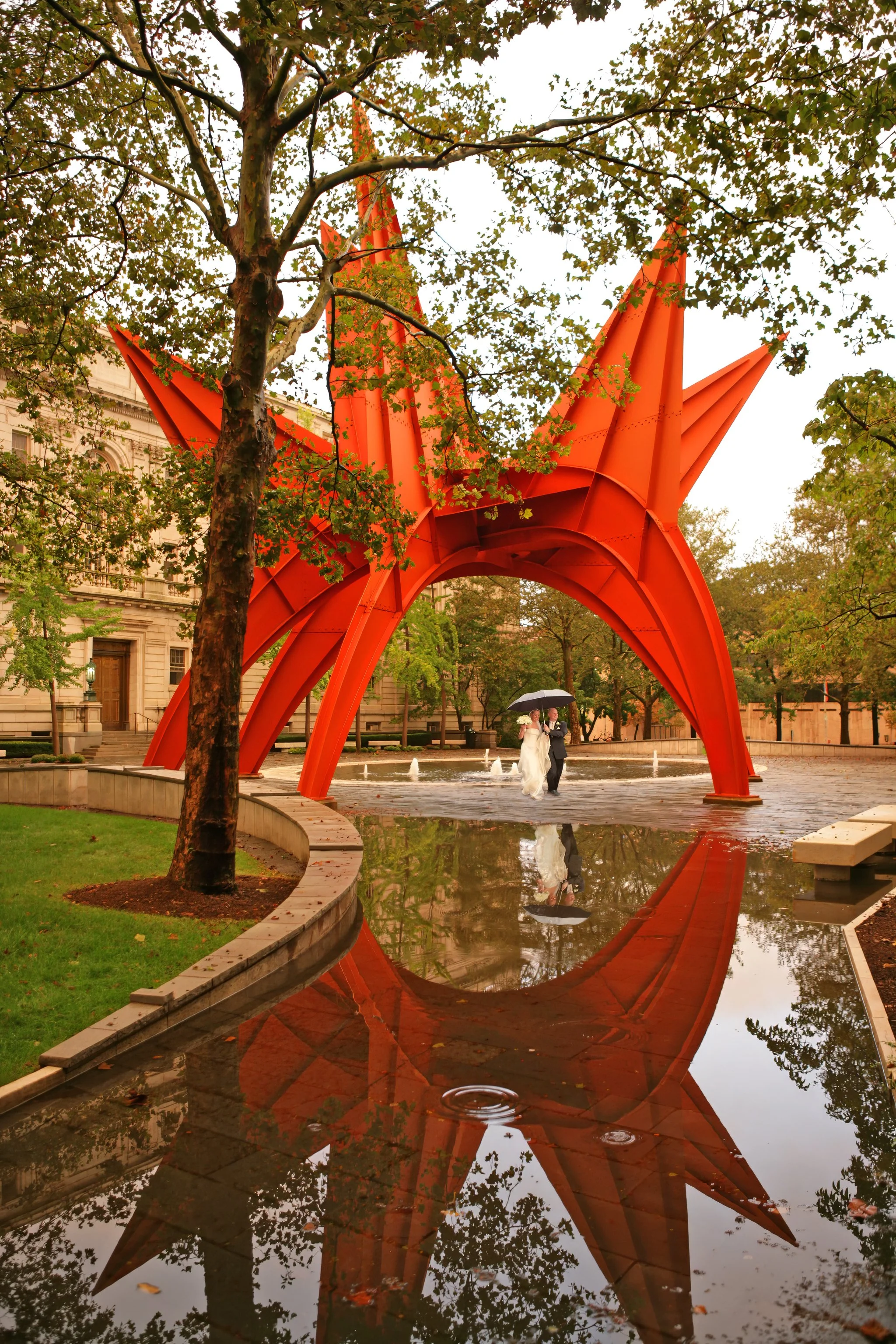 Bride and groom walking under an umbrella through Burr Mall next to the Wadsworth Atheneum in downtown Hartford Connecticut.