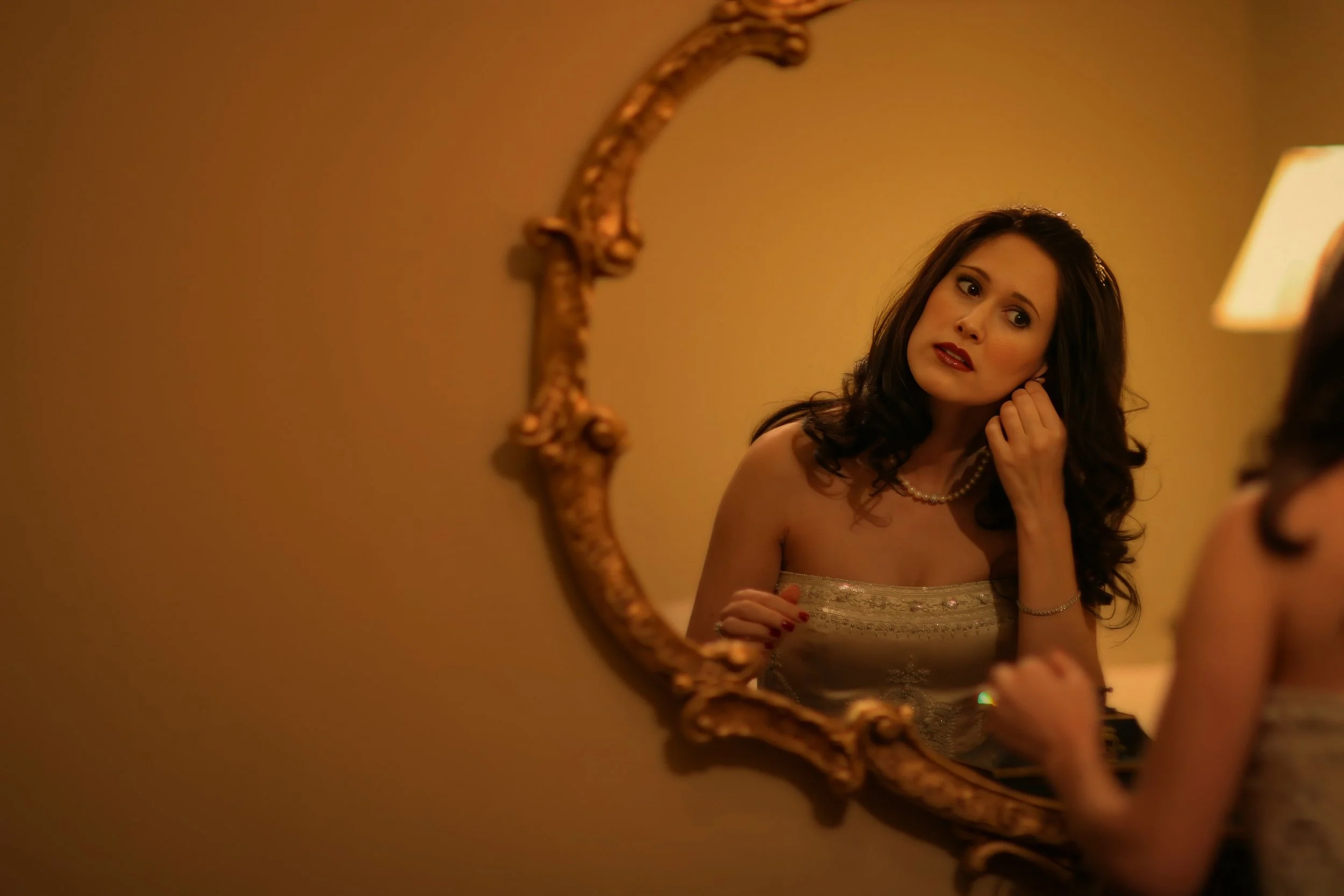 Bride putting on earrings in the mirror inside the bridal suite while preparing for her Oheka Castle wedding