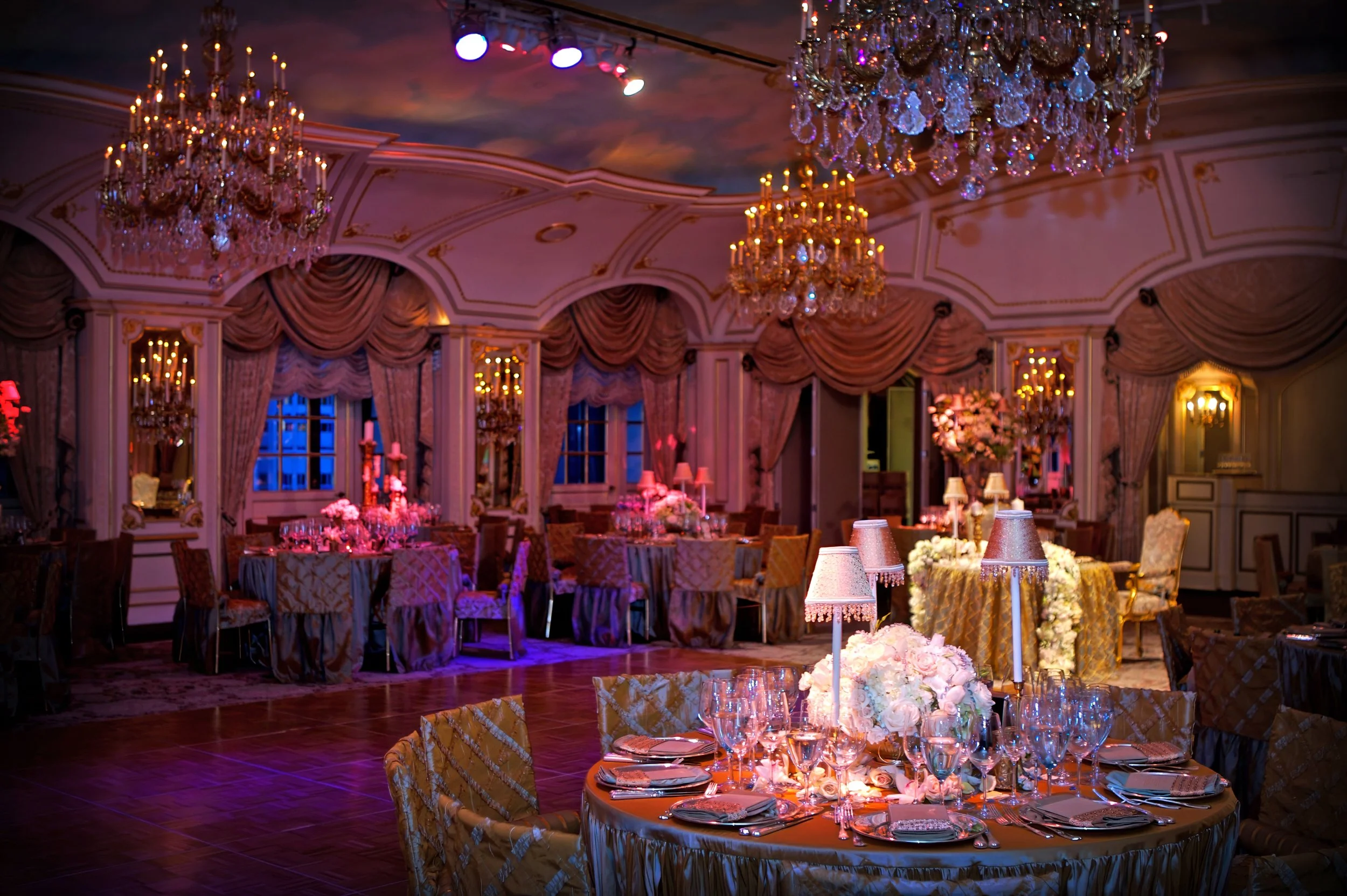 Floral arrangements, chandeliers, and candlelight decorating the ballroom for a wedding reception at The St. Regis New York.