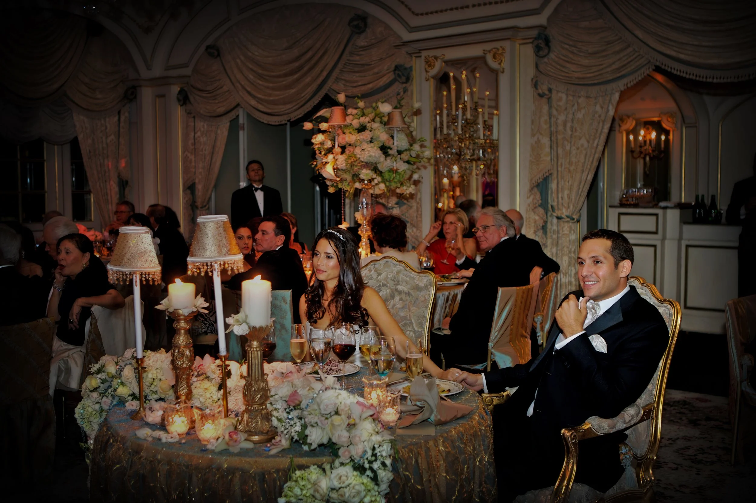 Bride and groom holding hands at their sweetheart table while listening to wedding toasts at The St. Regis New York.
