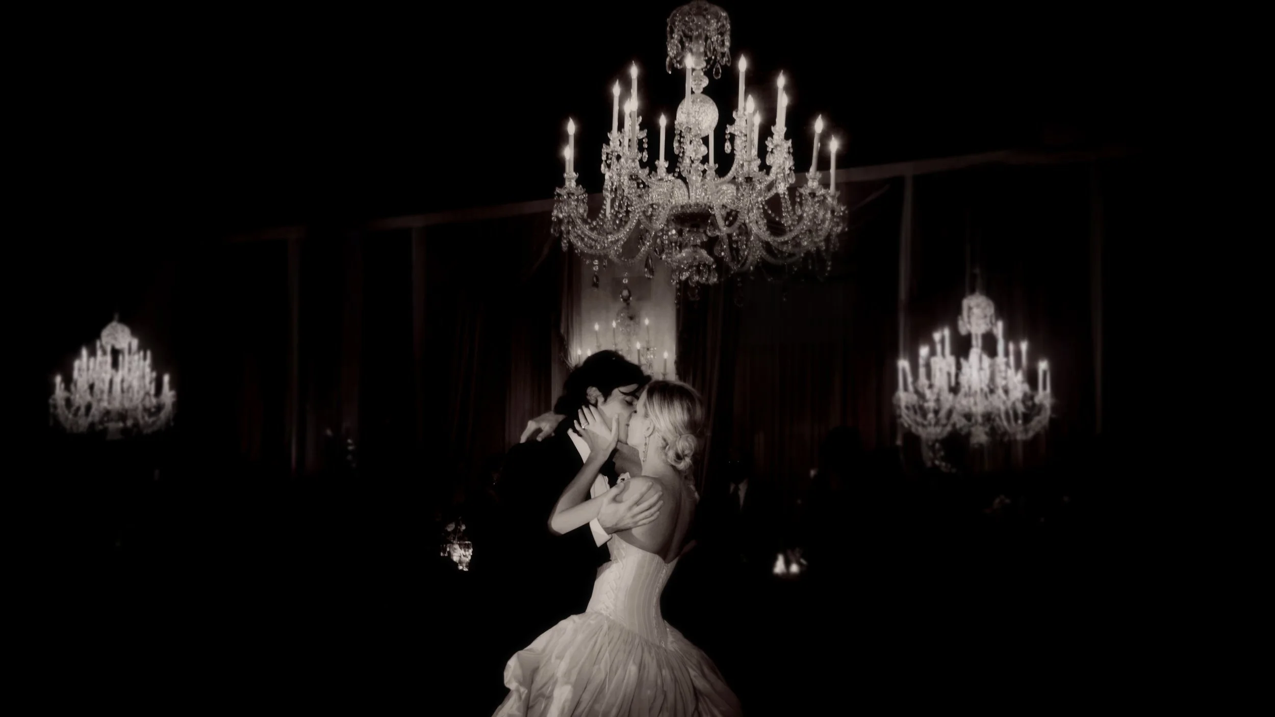 Bride and groom kissing beneath chandeliers in the ballroom at the Harmonie Club NYC