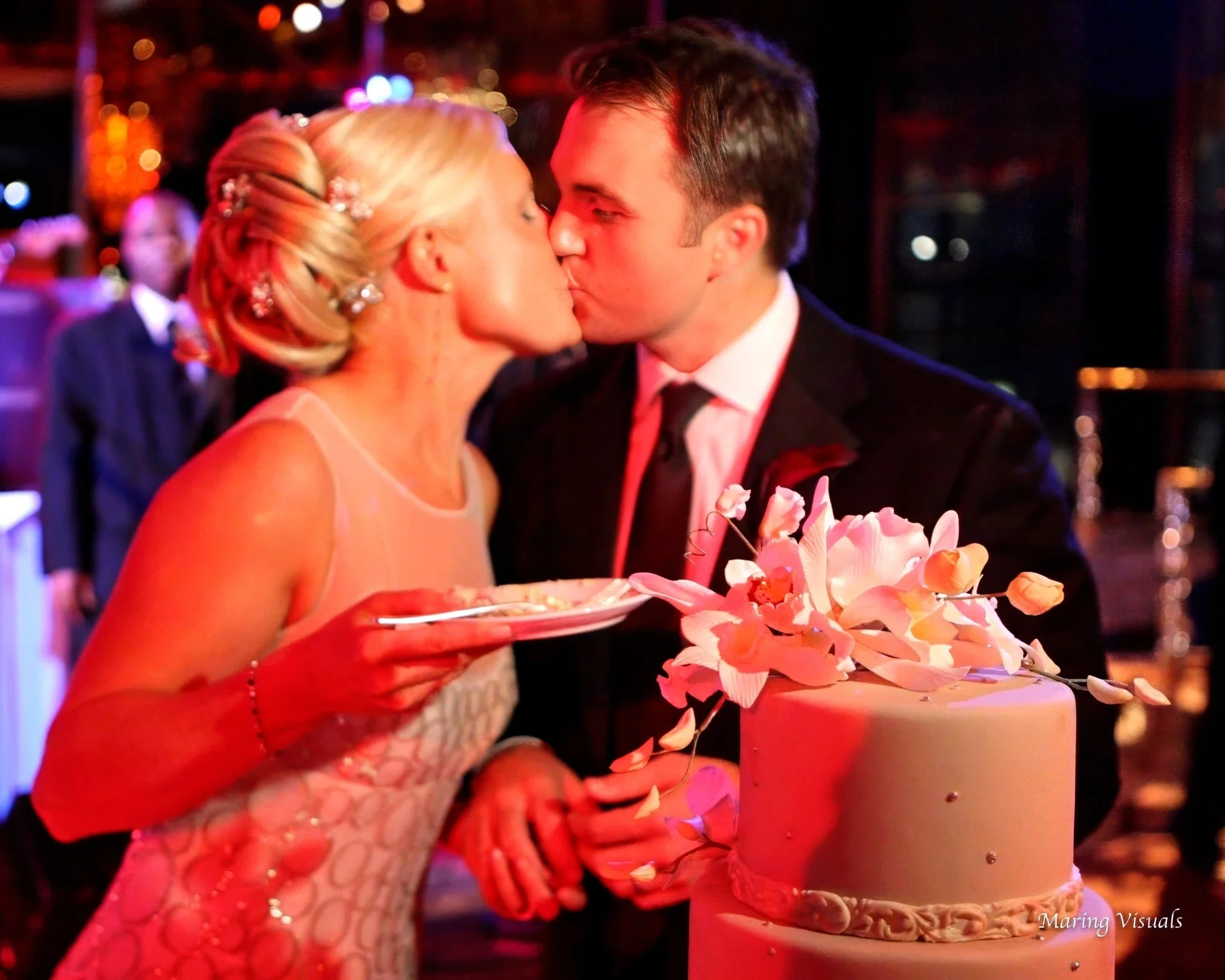 Bride and groom share a kiss after cutting their wedding cake during a Rainbow Room wedding reception in NYC.