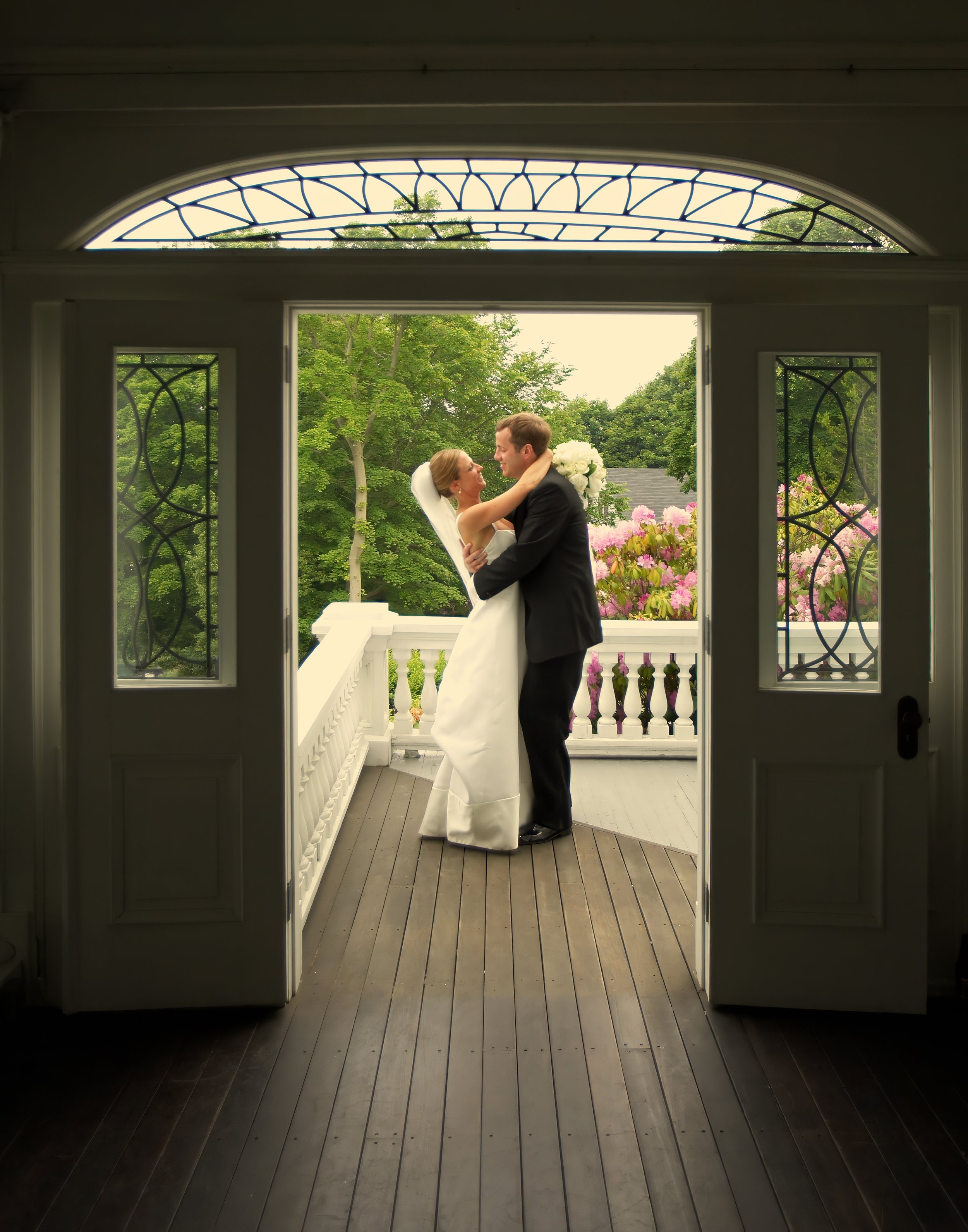 Bride and groom sharing a romantic moment on the porch of the Inn at Mystic framed through a doorway