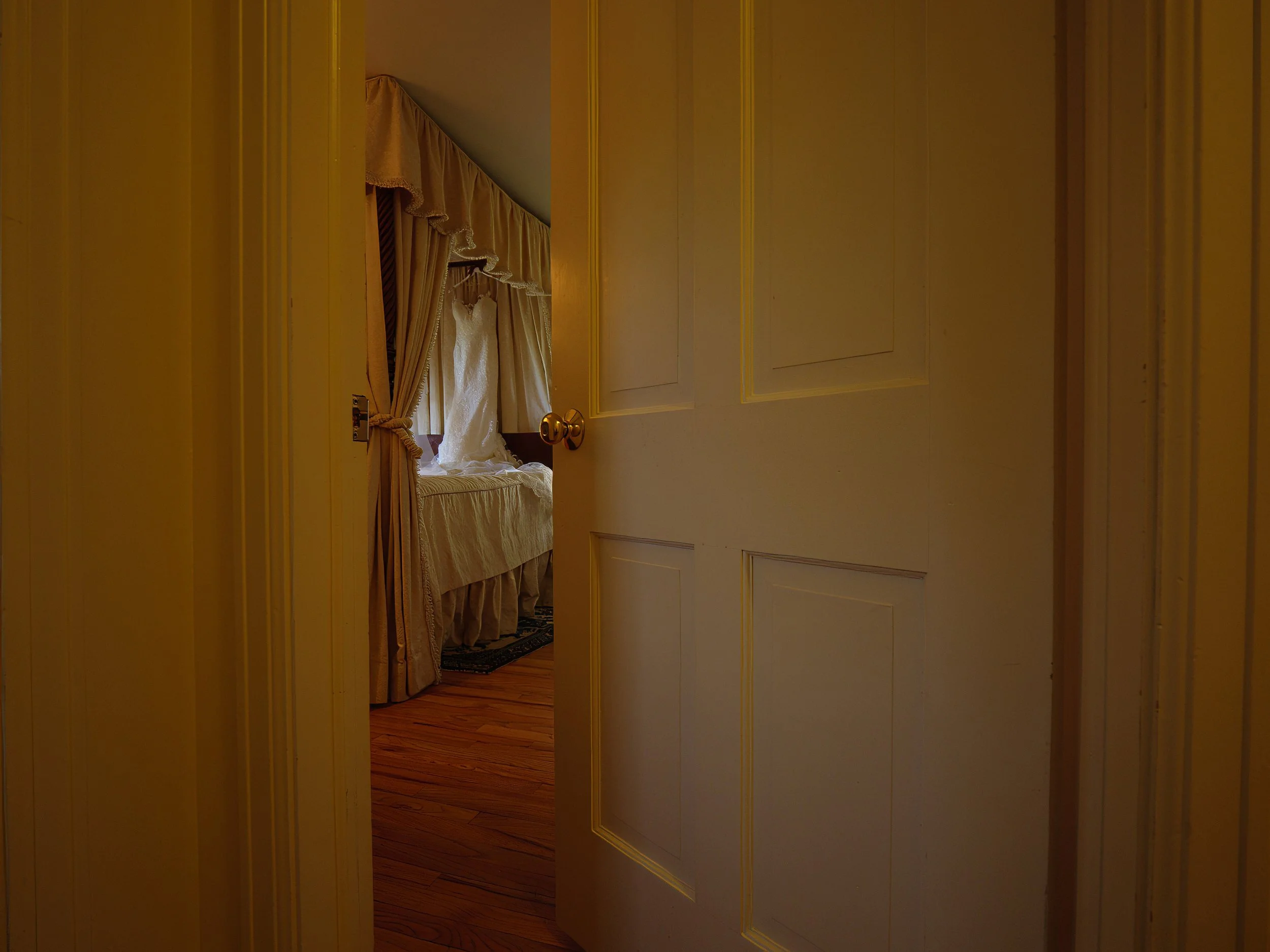 Wedding dress hanging on canopy bed in bridal suite at Lion Rock Farm photographed through doorway