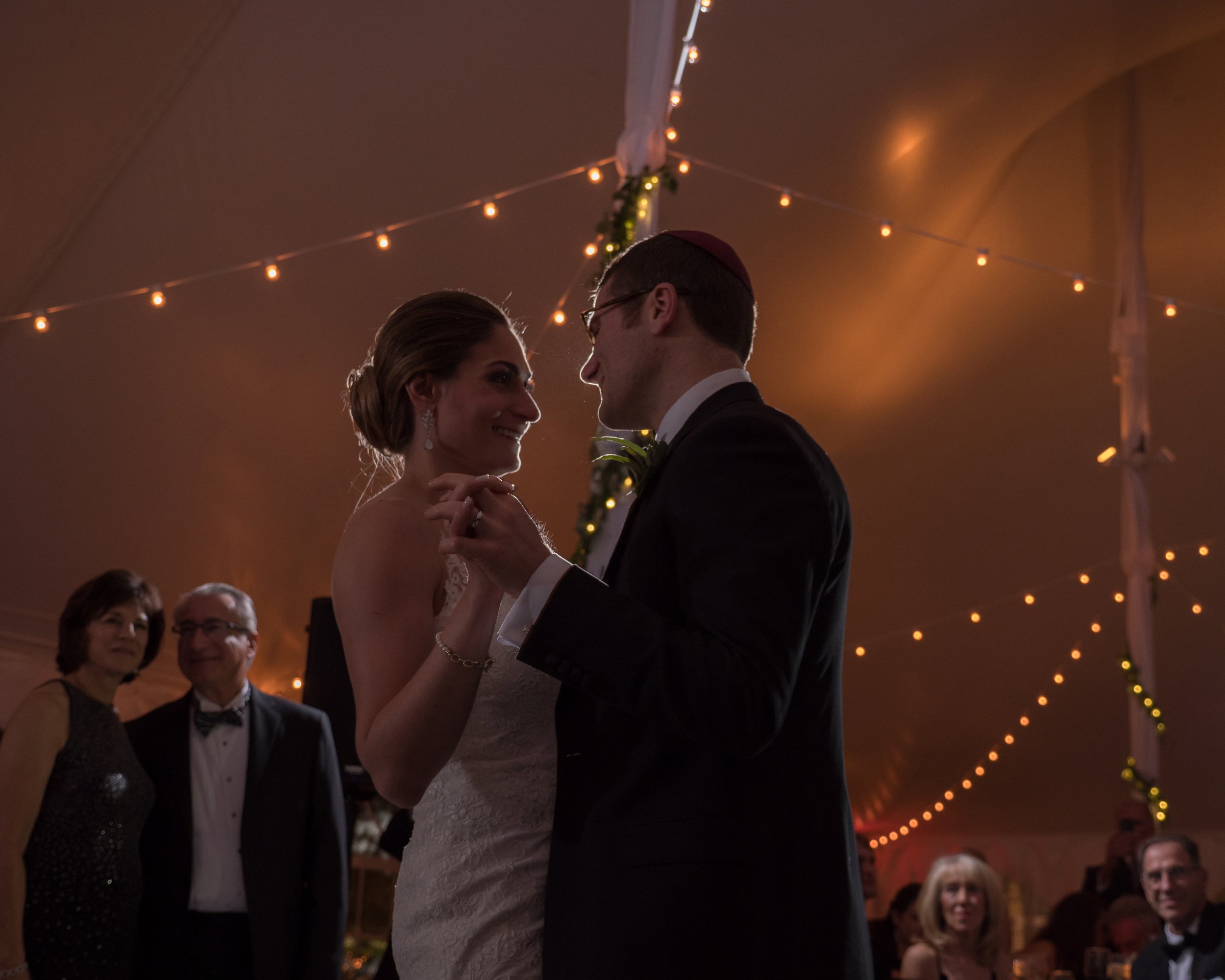 Bride and groom share a romantic first dance under glowing tent lights at a Lion Rock Farm wedding reception with soft rim lighting.