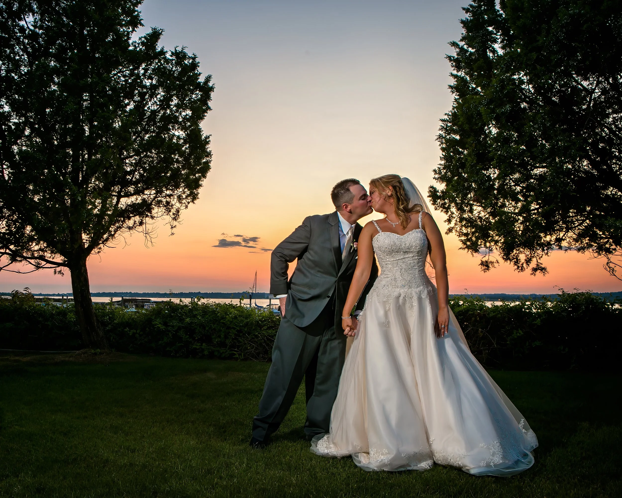 Bride and groom kiss at sunset on the lawn at Amarante’s Sea Cliff overlooking New Haven Harbor
