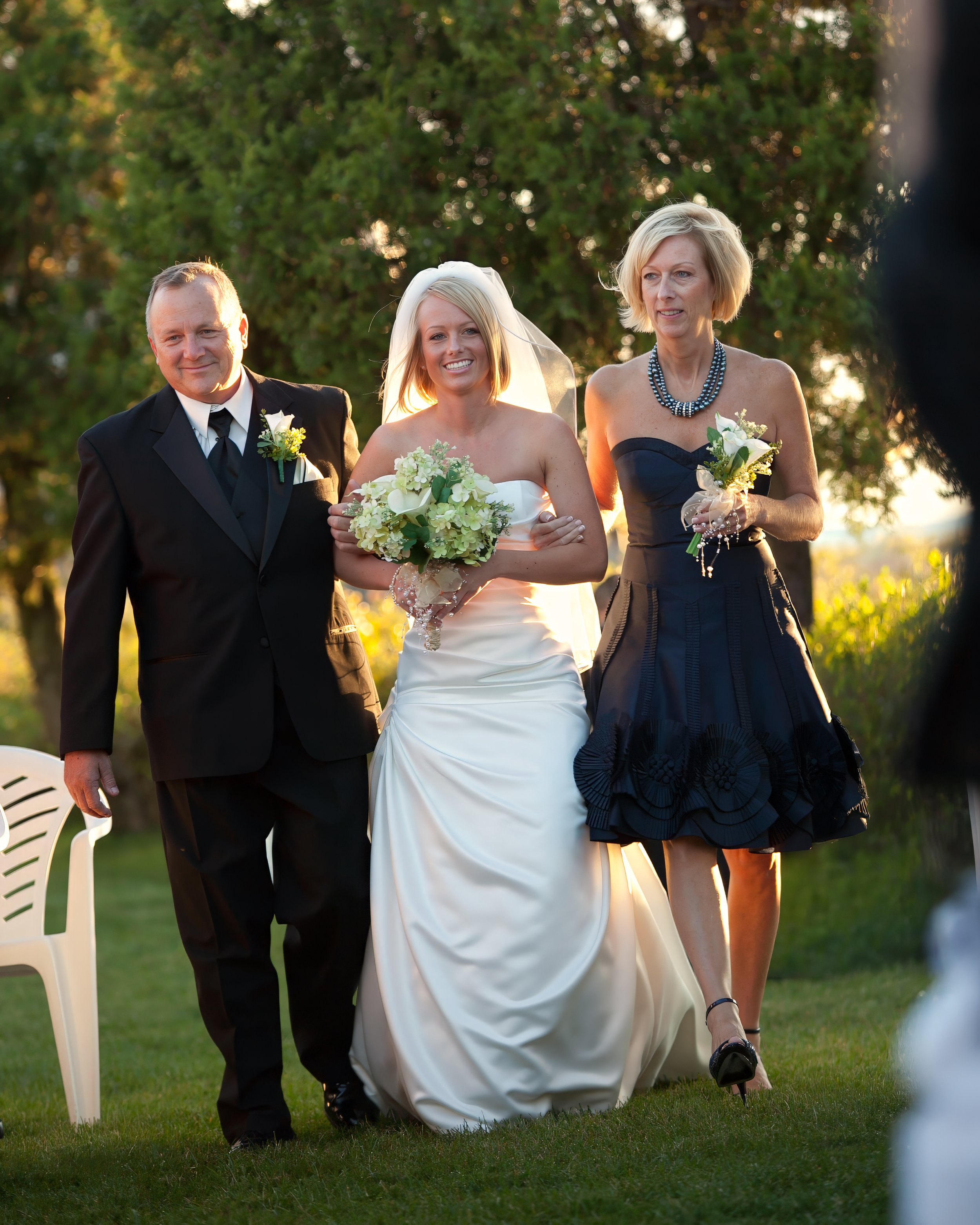 Bride walks down the aisle with her parents during an outdoor wedding ceremony on the lawn at Amarante’s in New Haven CT