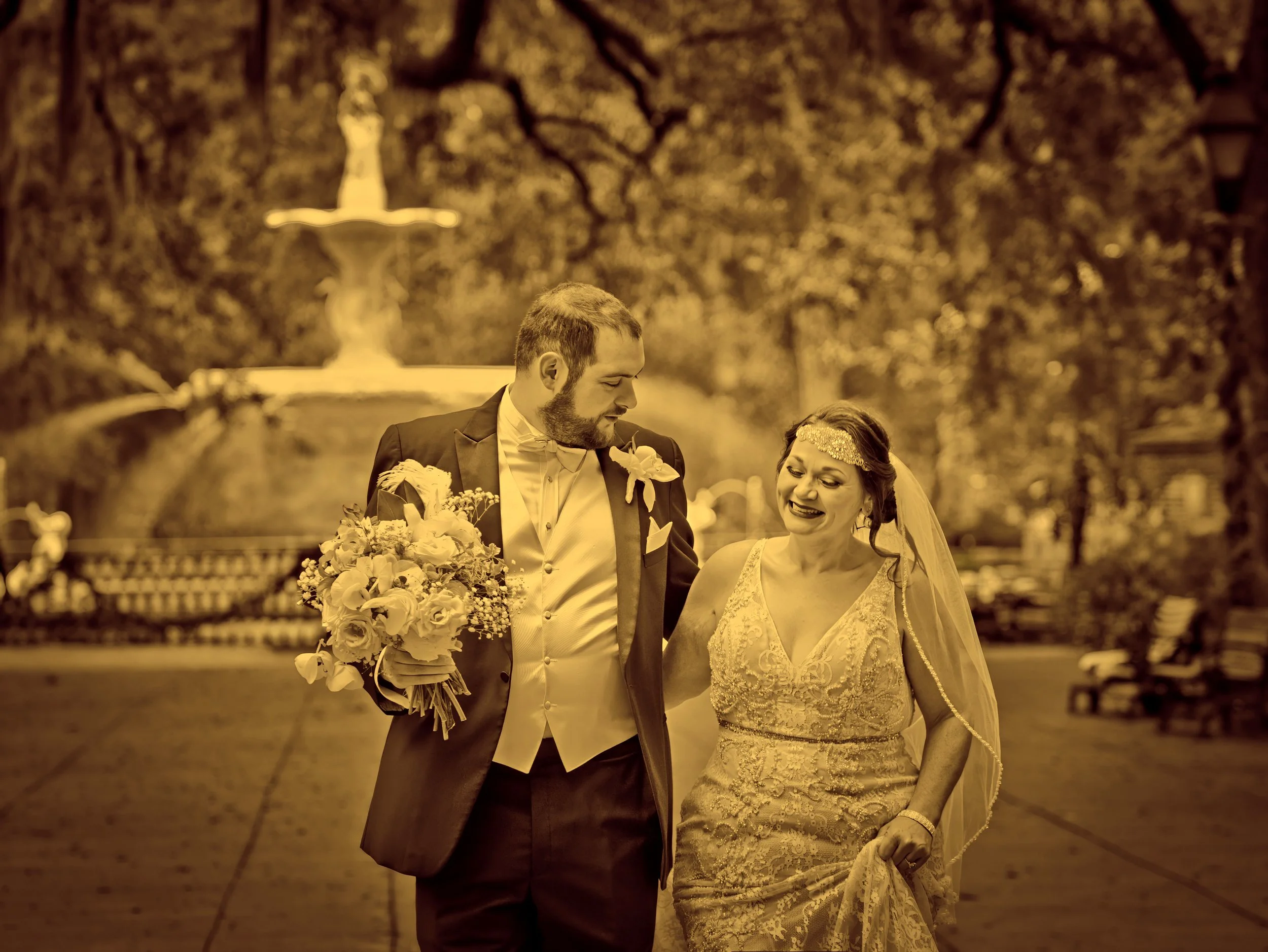 Bride and groom walk down Forsyth Park promenade joyfully with the historic fountain visible in the distance in Savannah, Georgia.