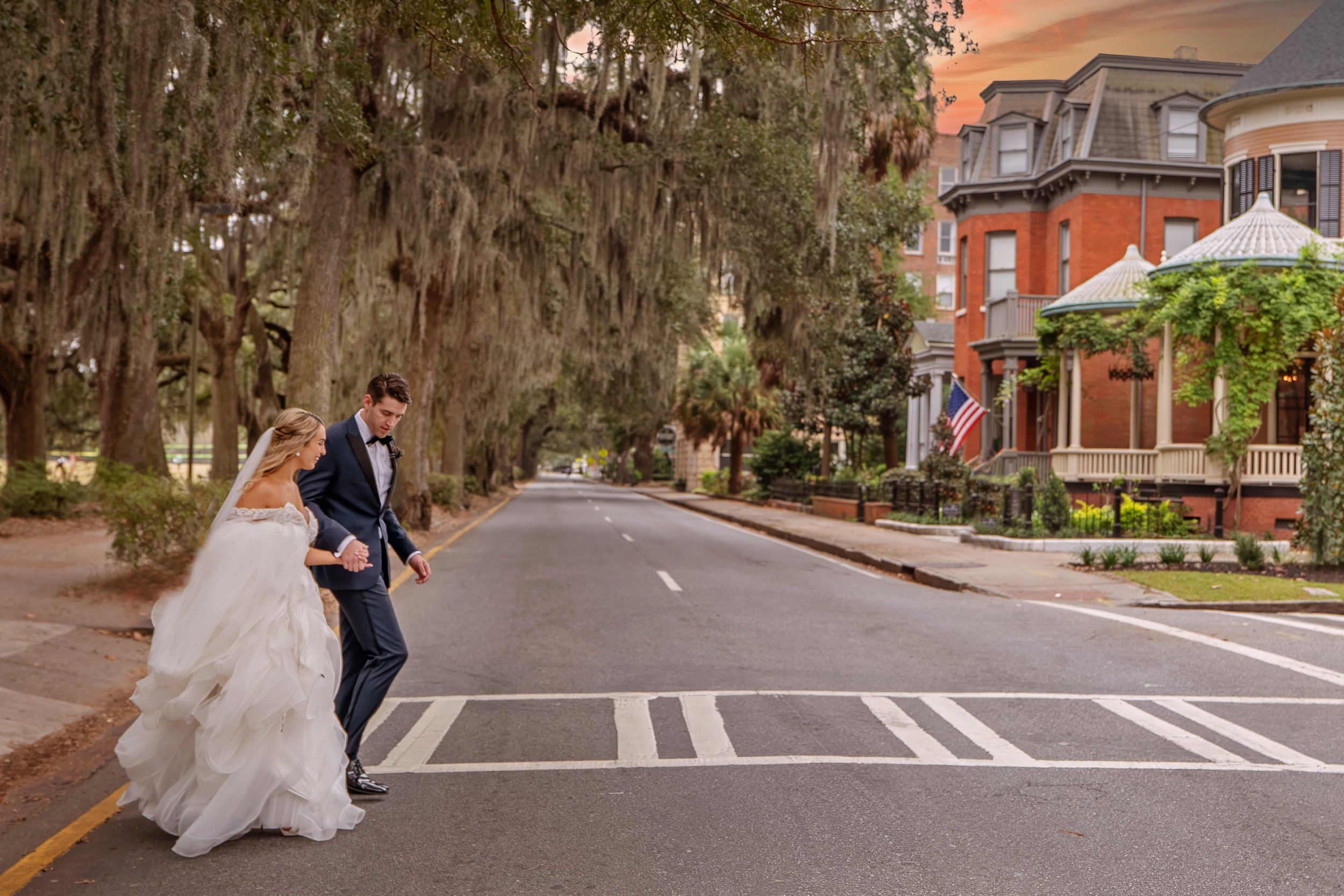 Bride and groom cross Whitaker Street from Forsyth Park with historic homes lining the street in Savannah.