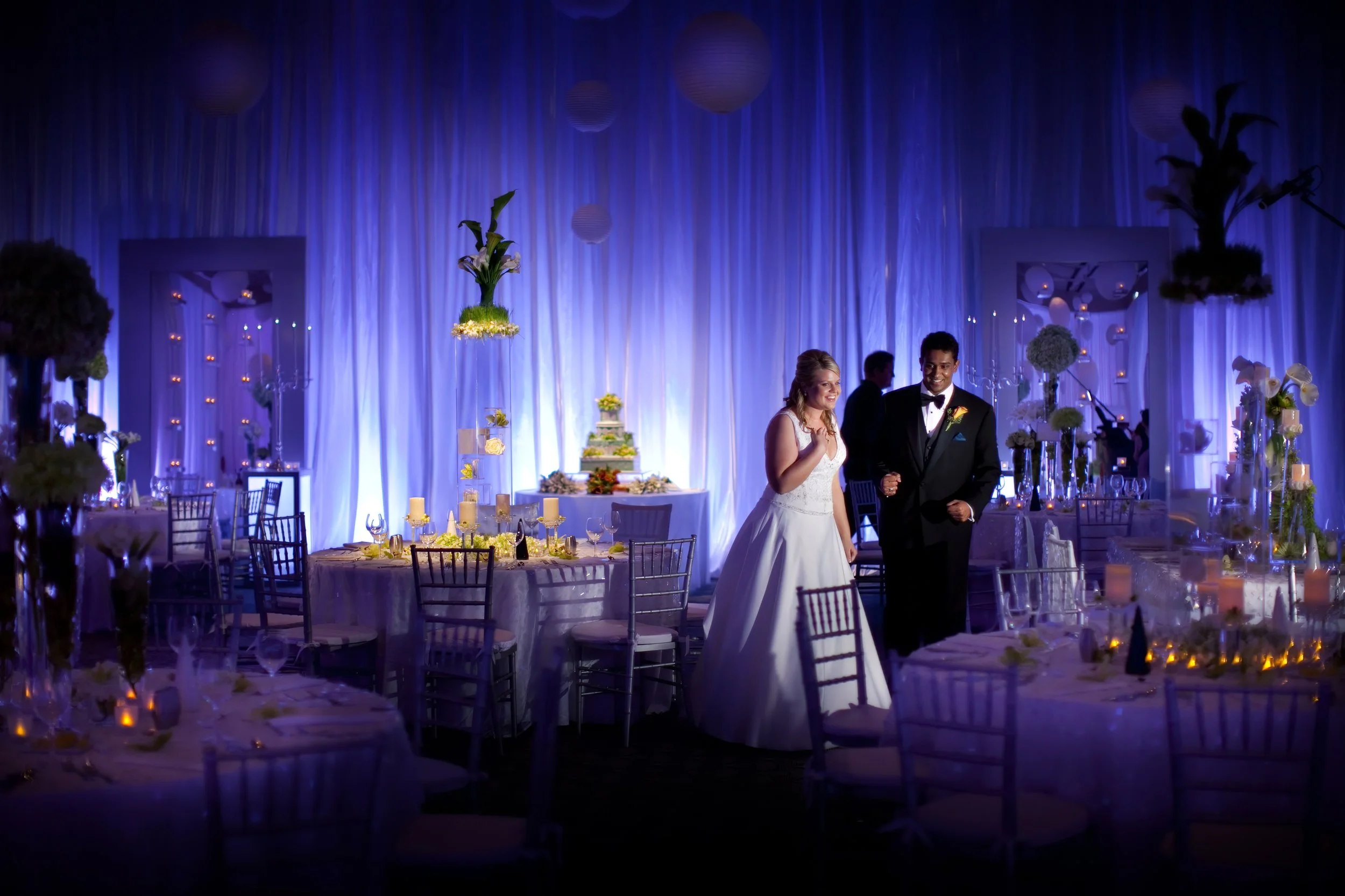 Bride and groom react with awe to the reveal of their luxury ballroom decor at a Disney Dream Wedding reception.