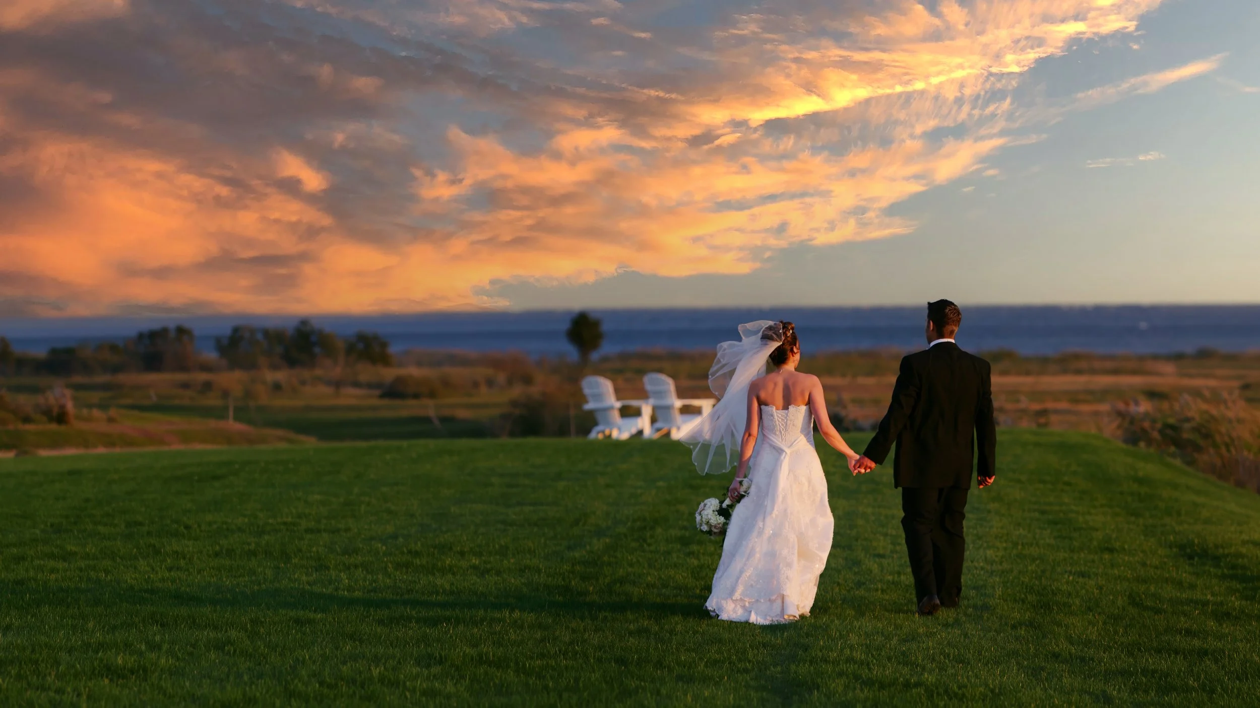 Bride and groom walk hand in hand toward the sunset overlooking Long Island Sound during their wedding reception at Guilford Yacht Club.