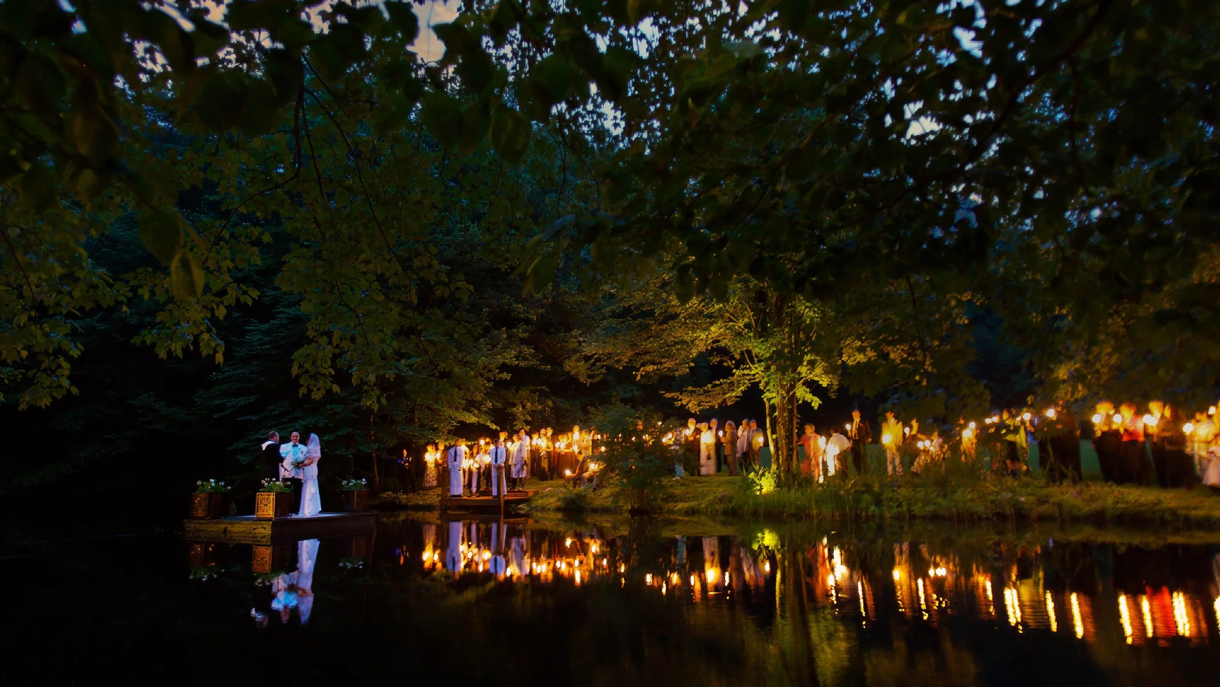 Bride and groom exchanging vows on a dock at a Connecticut estate wedding while guests hold candles along the shoreline.