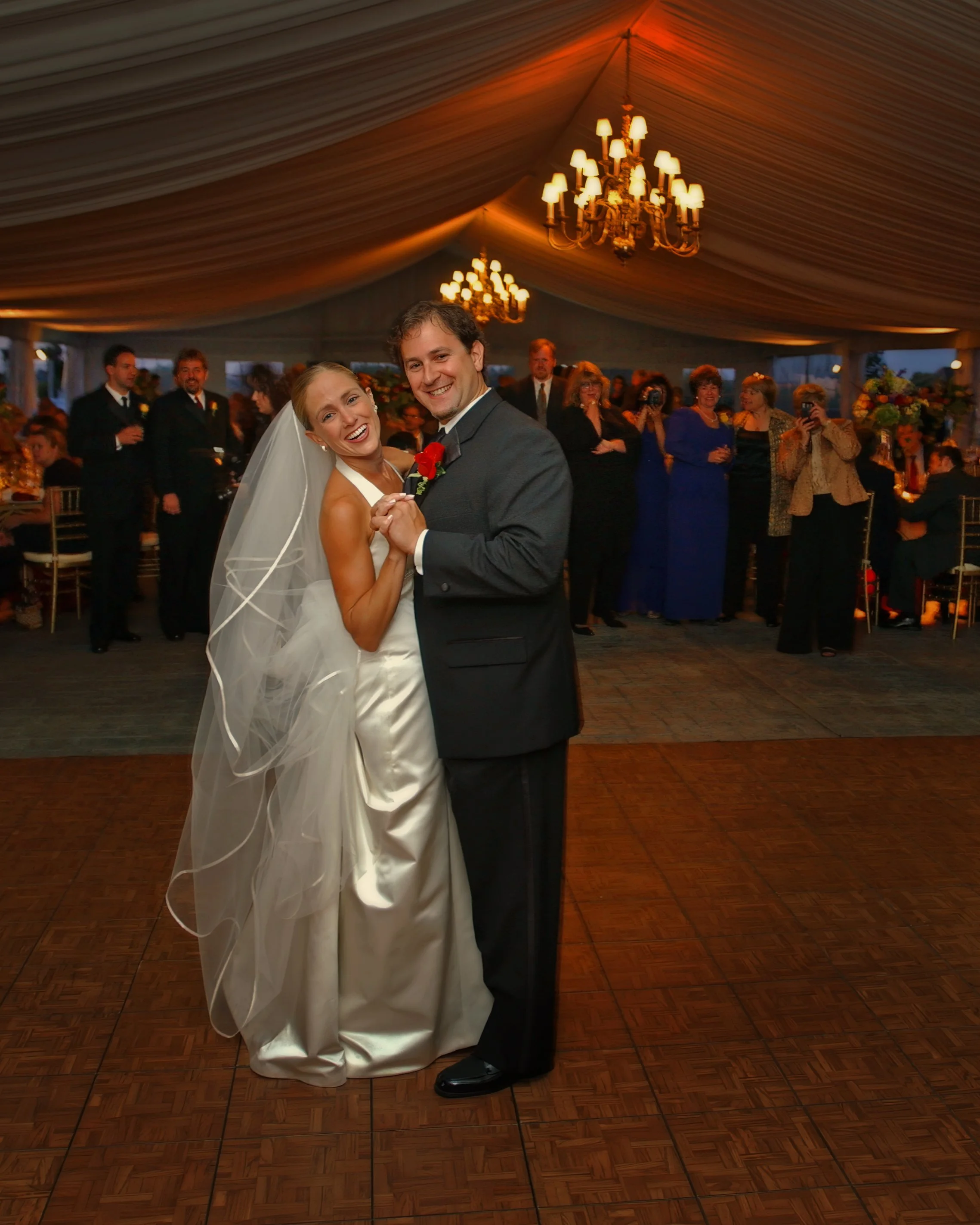Bride and groom smiling during first dance under warm tented reception lighting at Castle Hill.