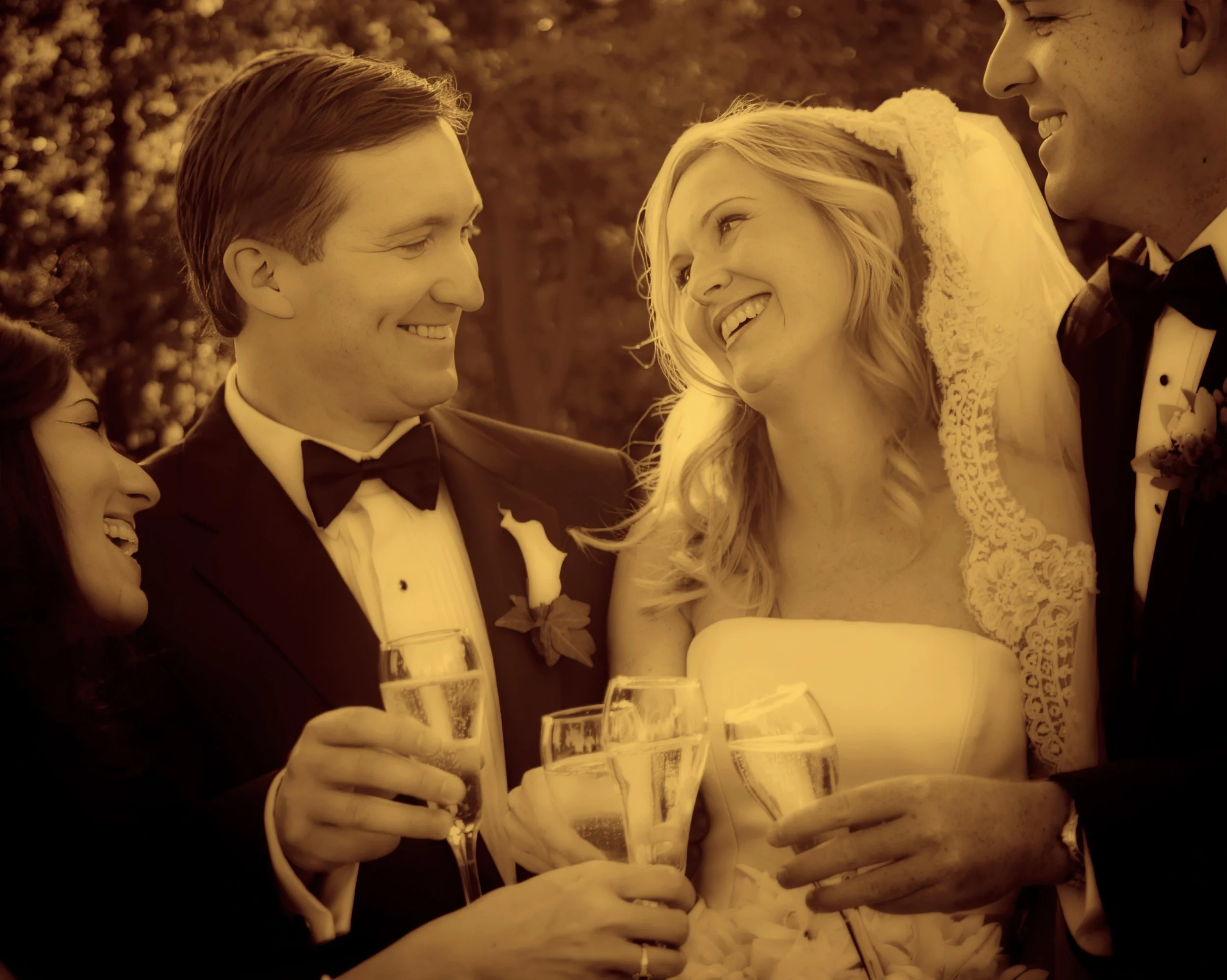 Bride and groom exchange joyful glances while raising champagne glasses with friends during their wedding celebration.