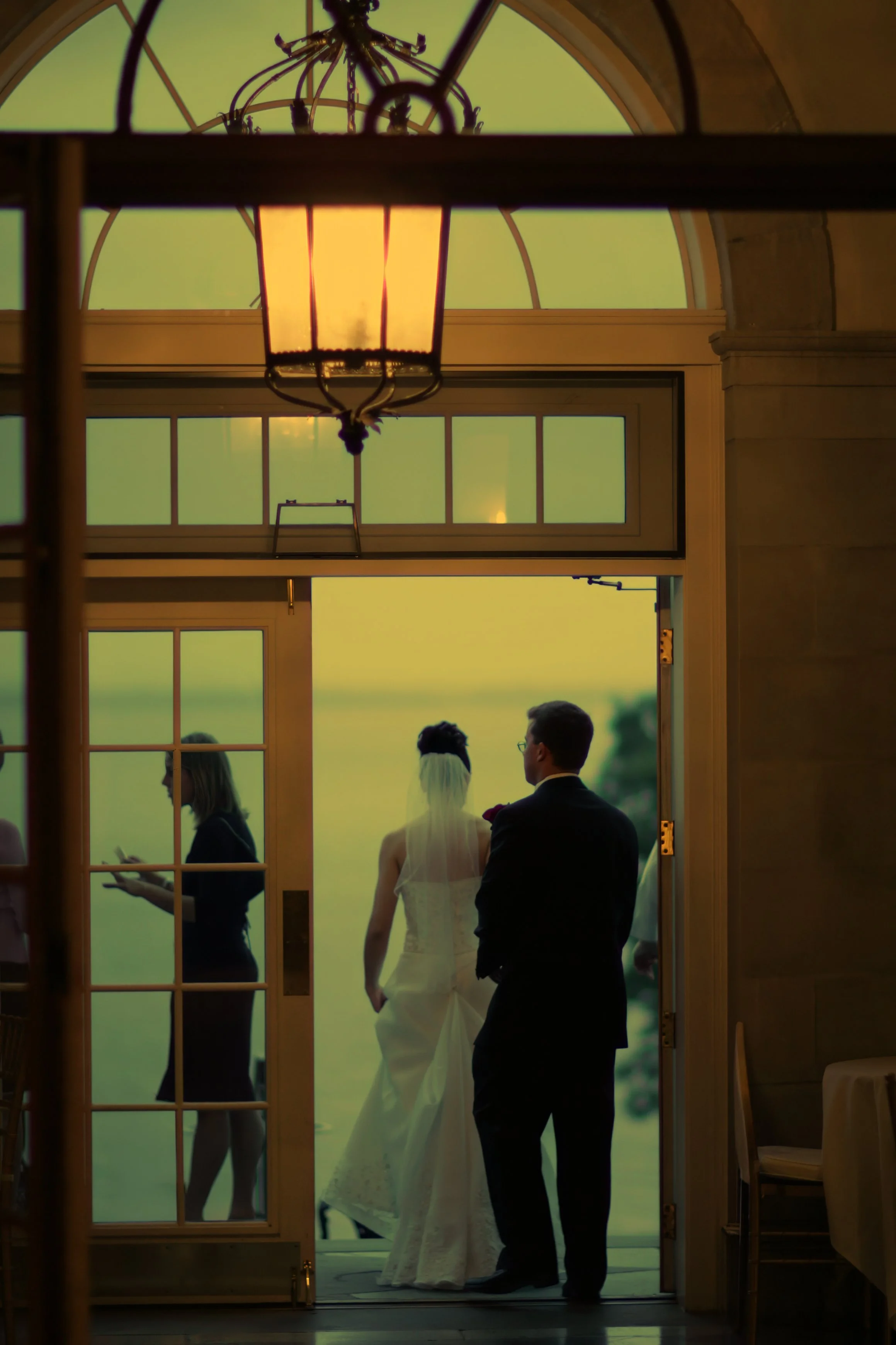 Bride and groom stepping onto the Aldrich Mansion patio during a warm summer evening reception.
